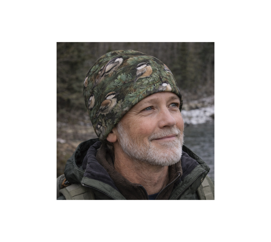 Elderly man in nature wearing a bamboo-lined beanie with collage of four different chickadees design with a green background.