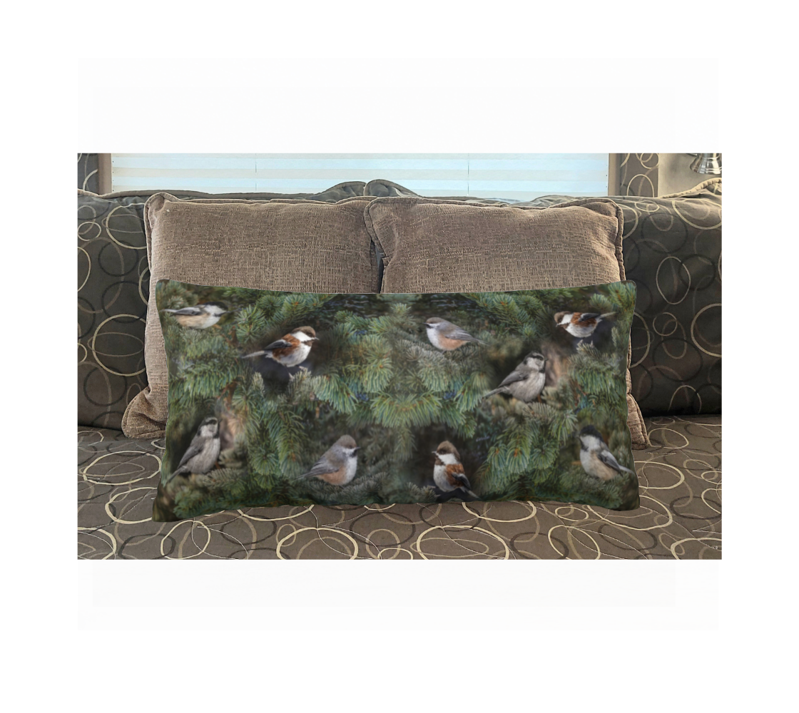 A 12 x 24 inch plush velveteen cushion cover featuring a photo of the 4 chickadees of Western Canada on a background of green pine boughs. This image is of the cushion cover on a pillow form on a bed.