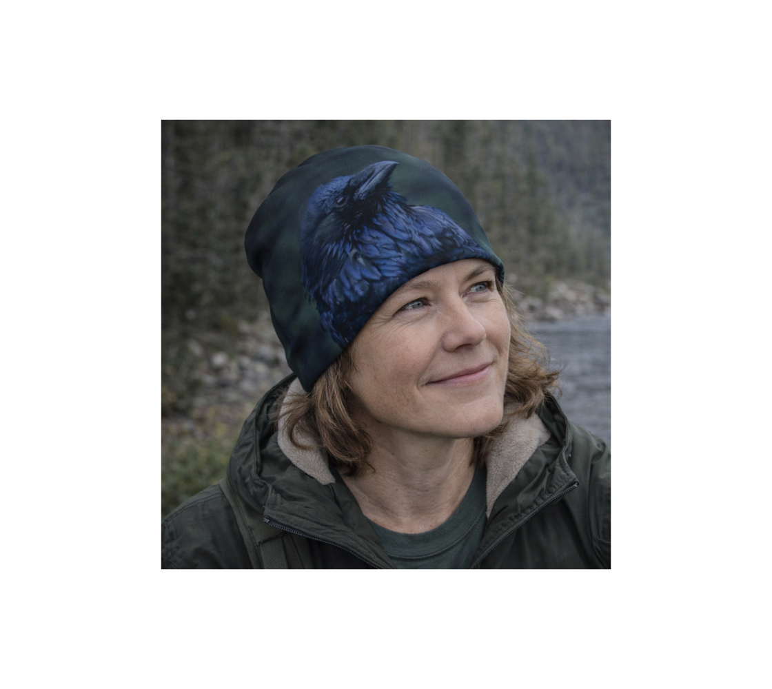 A woman standing by river wearing a beanie with an image of raven.