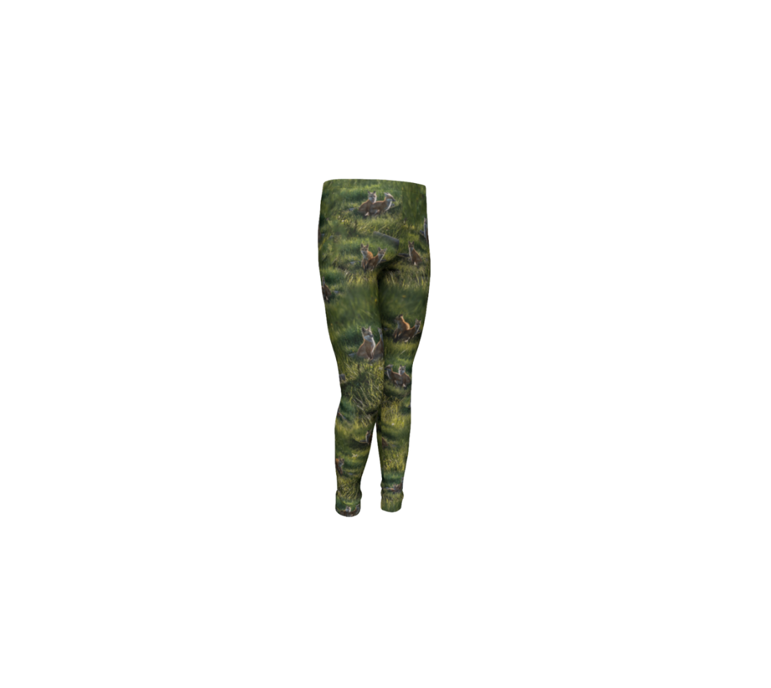 This is a front profile of a pair of kids leggings featuring a collage of photos of red fox kits. The background is green grass, with various images of the brown and white fox kits scattered throughout.