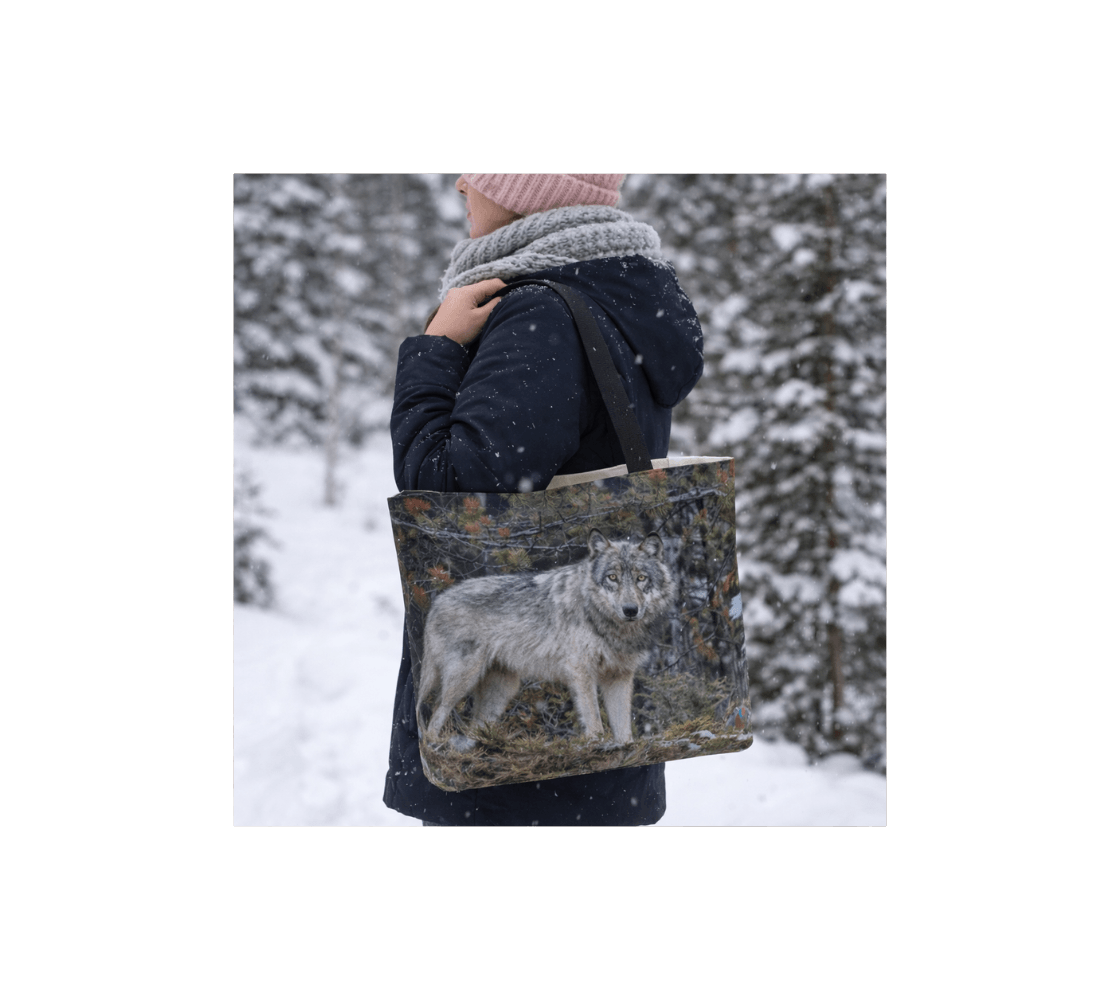 A woman carrying a gray wolf large reusable tote bag from our real wildlife photography standing in a snowy forest.