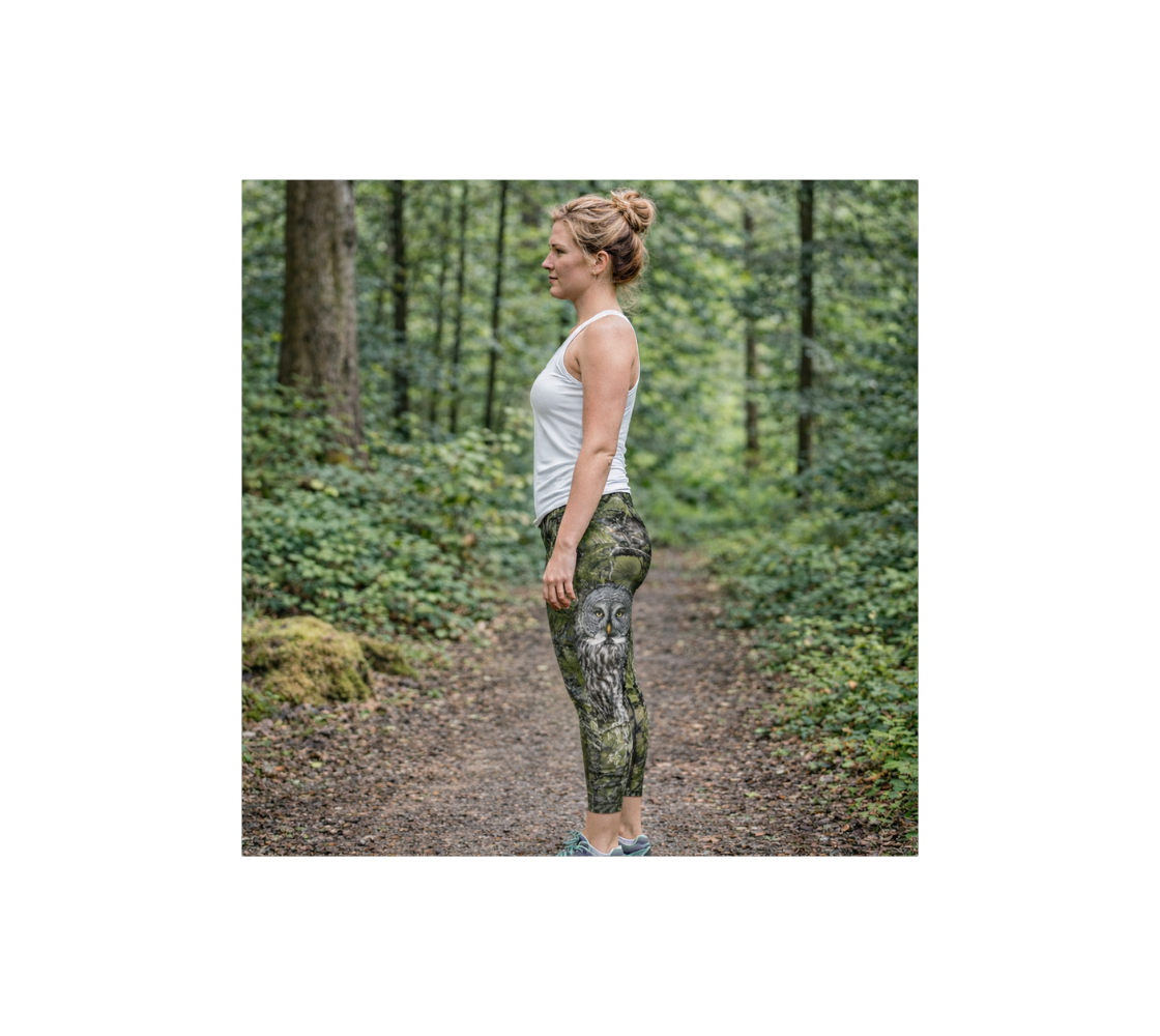 A woman standing on a path in a forest wearing a pair of great gray owl classic leggings from our real wildlife photography.