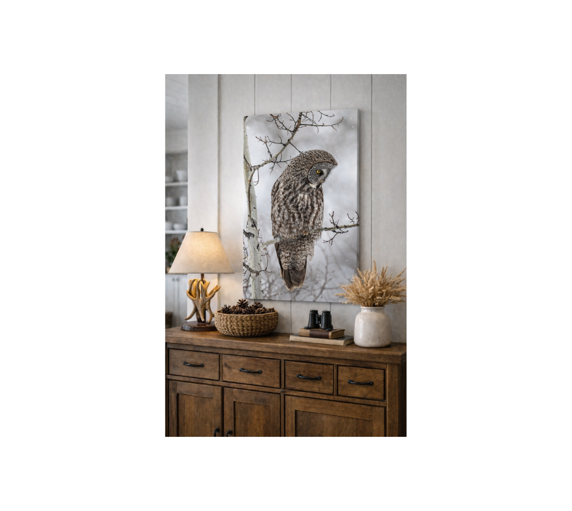 A portrait canvas print of our photograph featuring great gray owl on a branch with a foggy white background hanging on a white wall in a home setting.