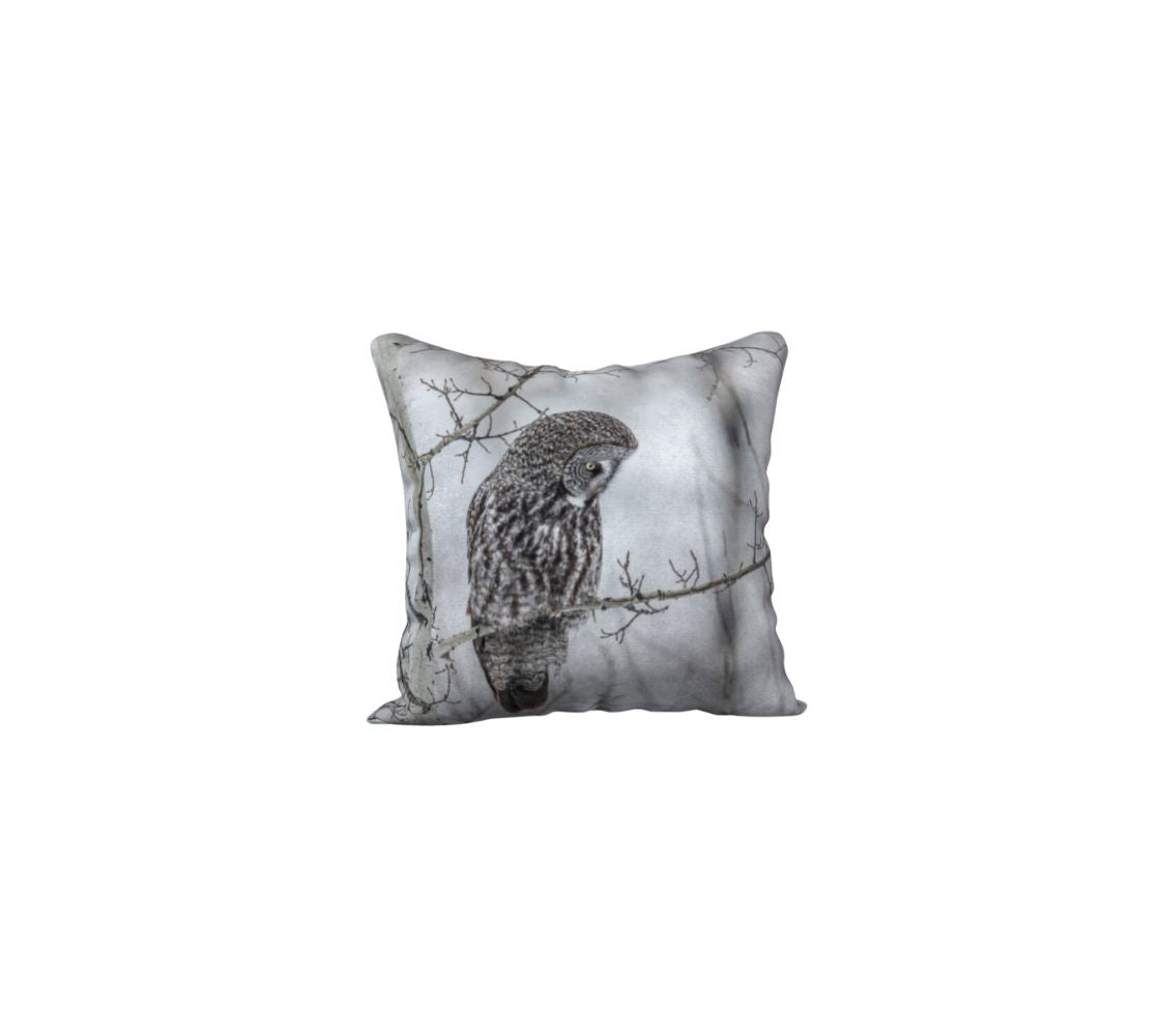 A 18 x 18 inch plush velveteen cushion cover features a photo of a great grey owl in the foggy morning. The background is white and grey, with blurred tree branches due to the fog and frost, with a great grey owl perched on branch.