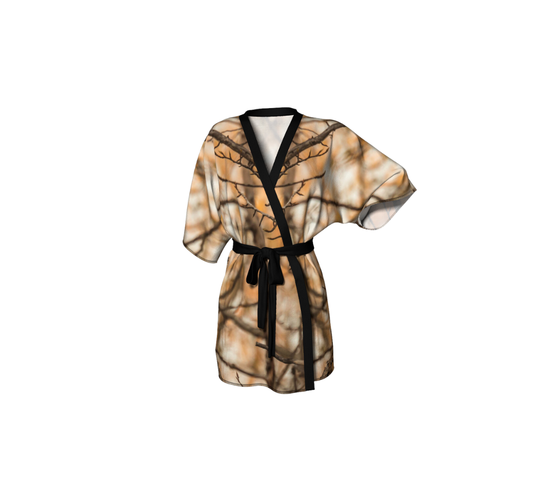 This frontview is of a semi-sheer poly chiffon kimono robe featuring a photo of branches. Background is of orange, brown and white blurred tree branches. Kimono has black trim with a lightweight bamboo black belt for tying.
