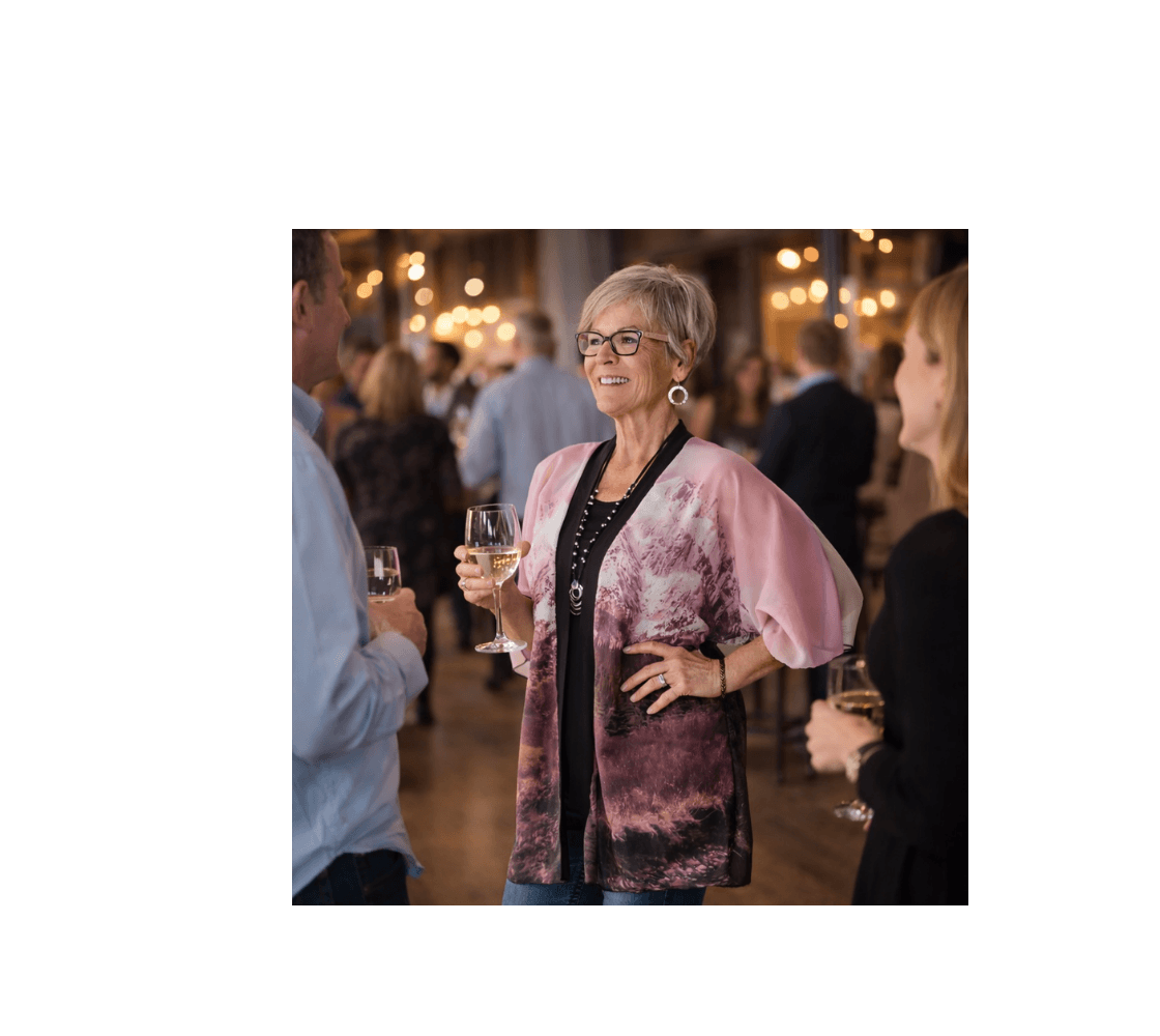 A woman wearing a pink mountain sunset kimono cover up from our nature photography holding a glass of win in a social setting.