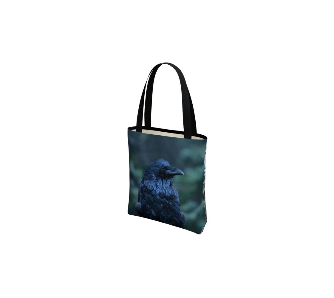 A small reusable tote bag with a portrait of a raven design with a mottle green background.