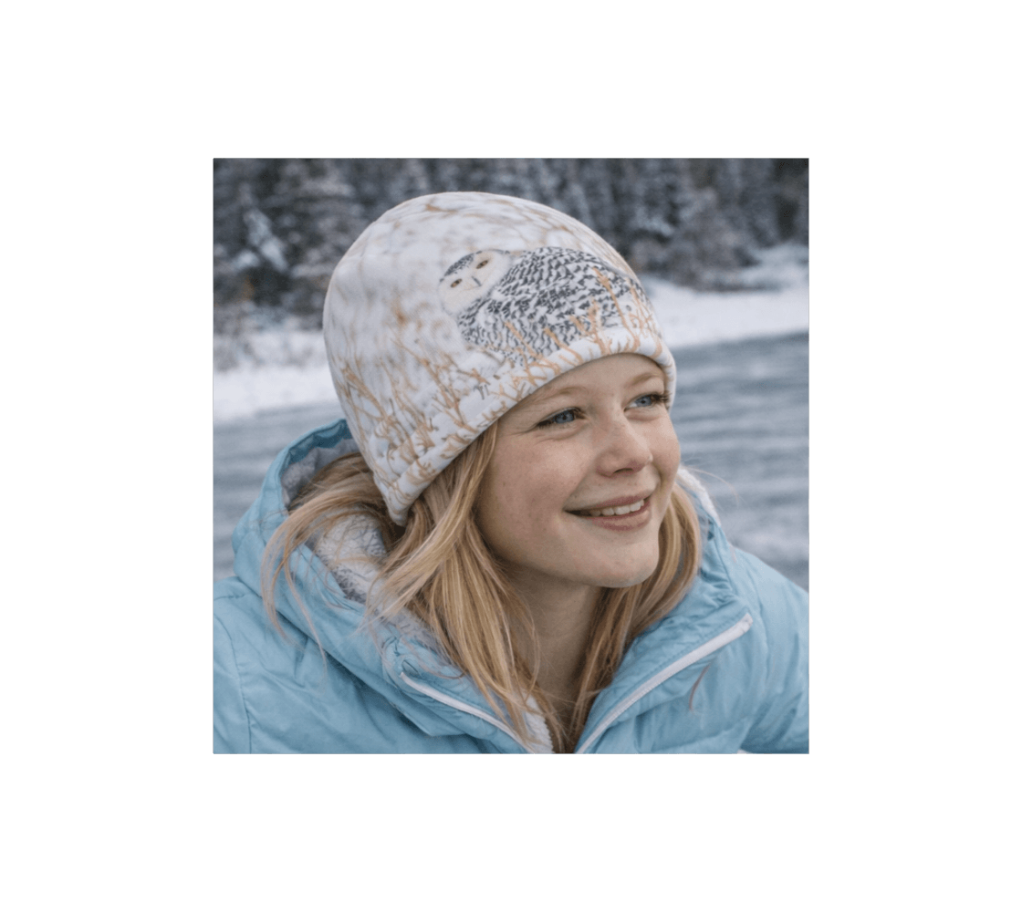 A young girl wearing a snowy owl bamboo-lined beanie from our real wildlife photography by snowy river bank.