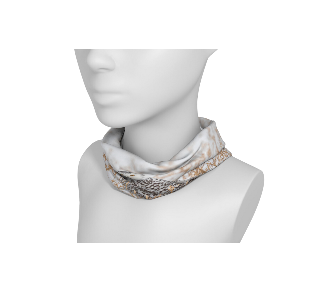 This is an image of photo of a snowy owl head and neck band worn as a neckband on a mannequin. The photo print is of a snowy owl looking at you. It is on the ground in a white snow covered field surrounded by gold colored field stubble sticking up out of the ground.