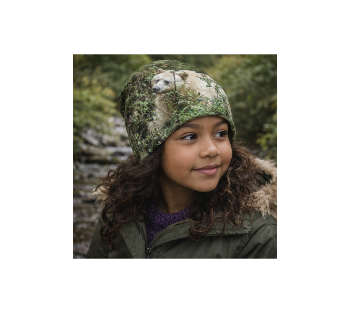 A young girl in nature wearing a bamboo-lined beanie with an image of spirit bear design with a green background.