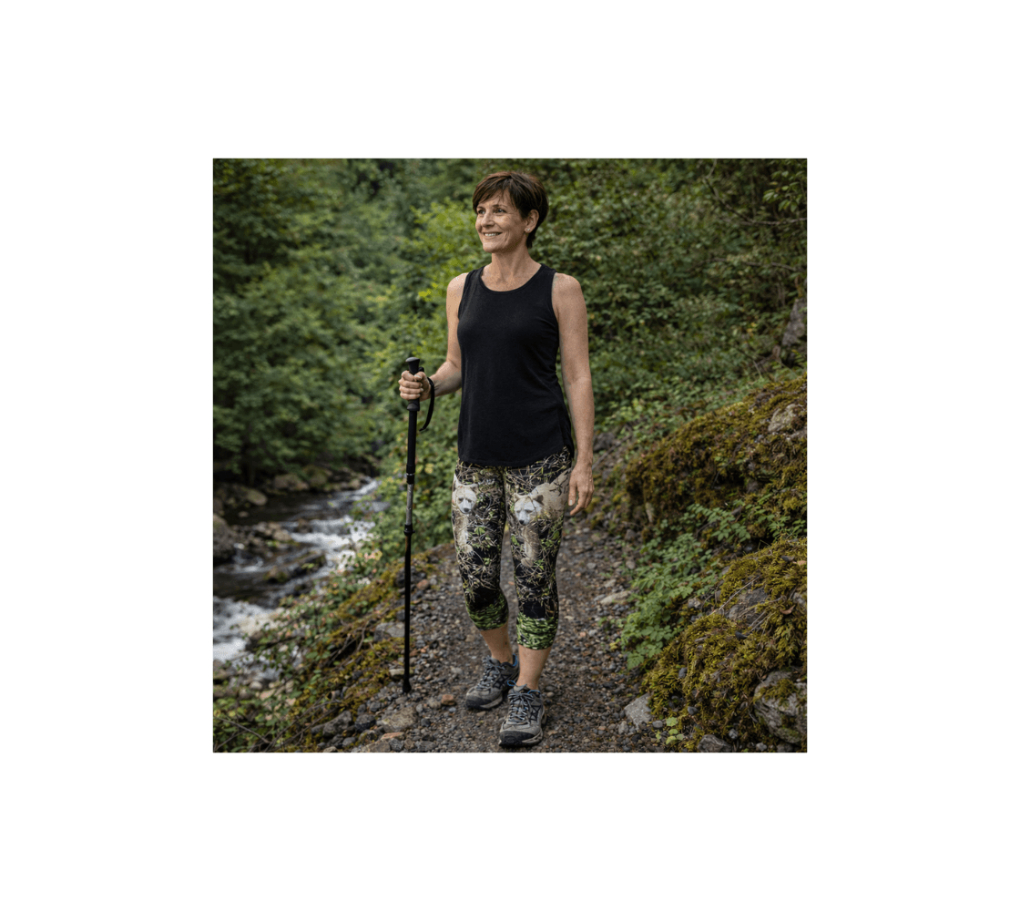 A woman hiking wearing a pair of spirit bear classic capri leggings from our wildlife photography standing by a stream.