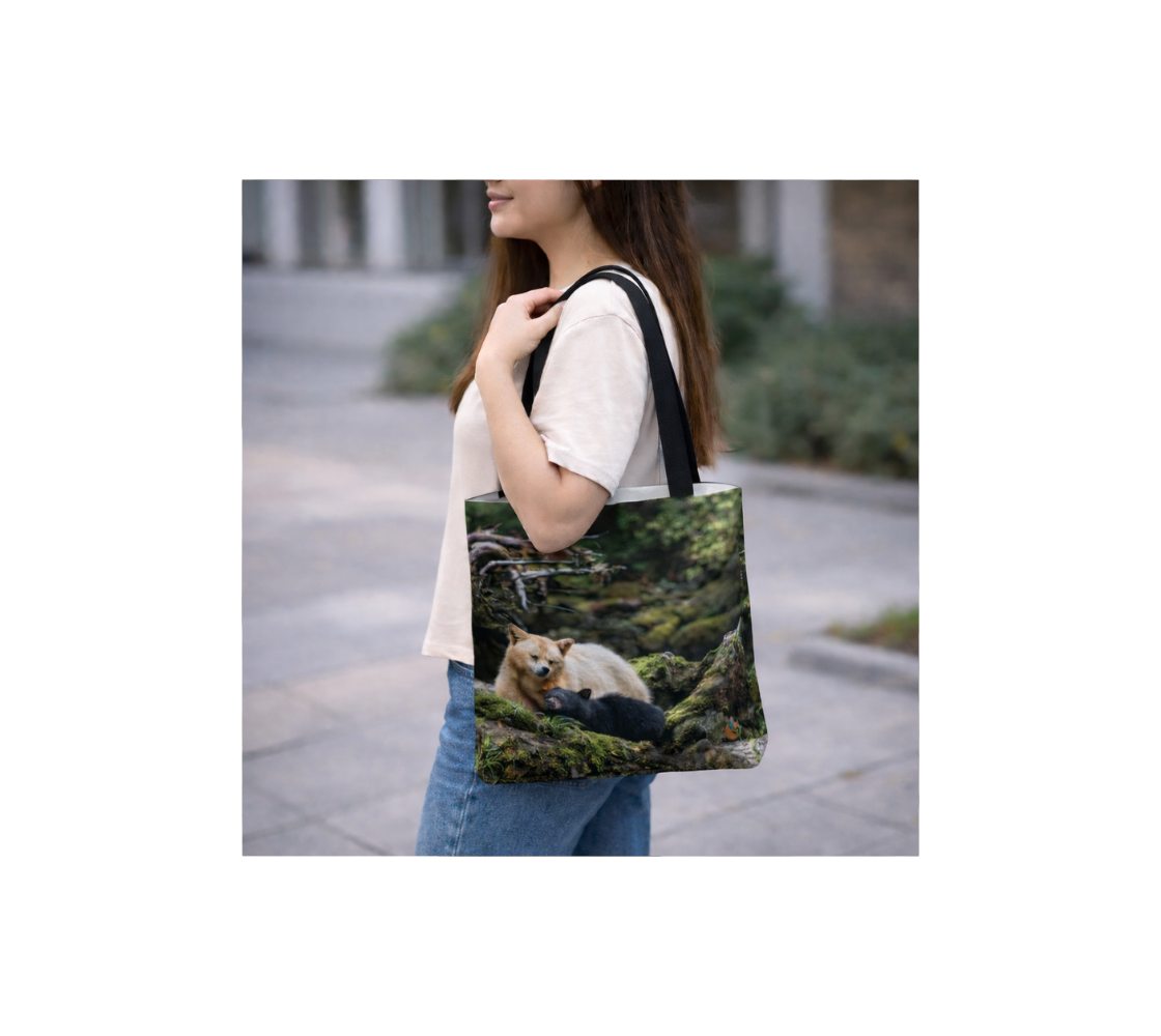 a woman holding a small reusable tote bag with an image of a spirit bear and cub design with a green background standing outdoors.