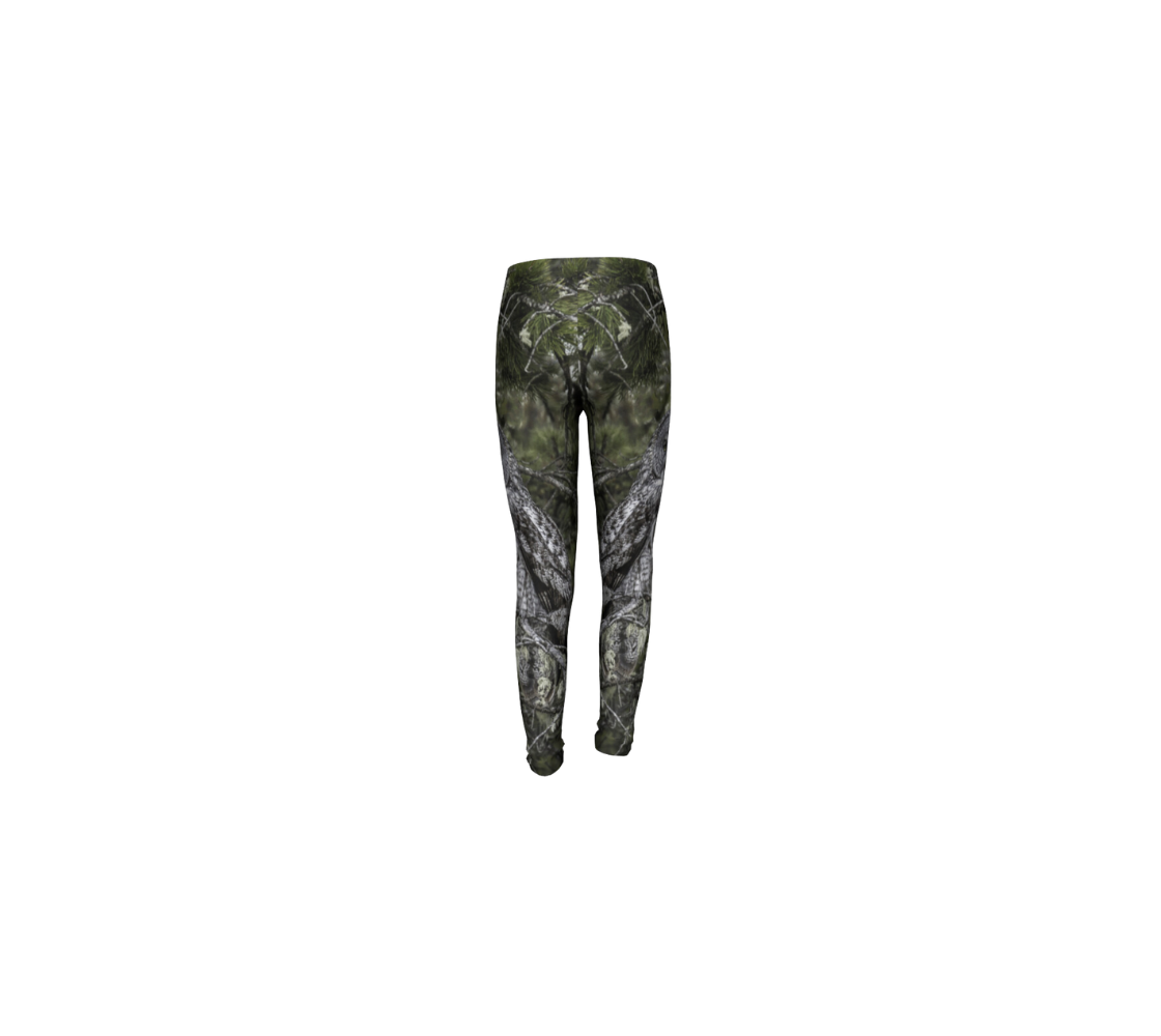 This is a rear profile of a pair of kids leggings with a photo of an owl on the side of each leg. The background is green pine boughs and lichen hanging from the grey pine tree branches, with a great grey owl with black, grey and white feathers, and yellow eyes, perched on a branch.