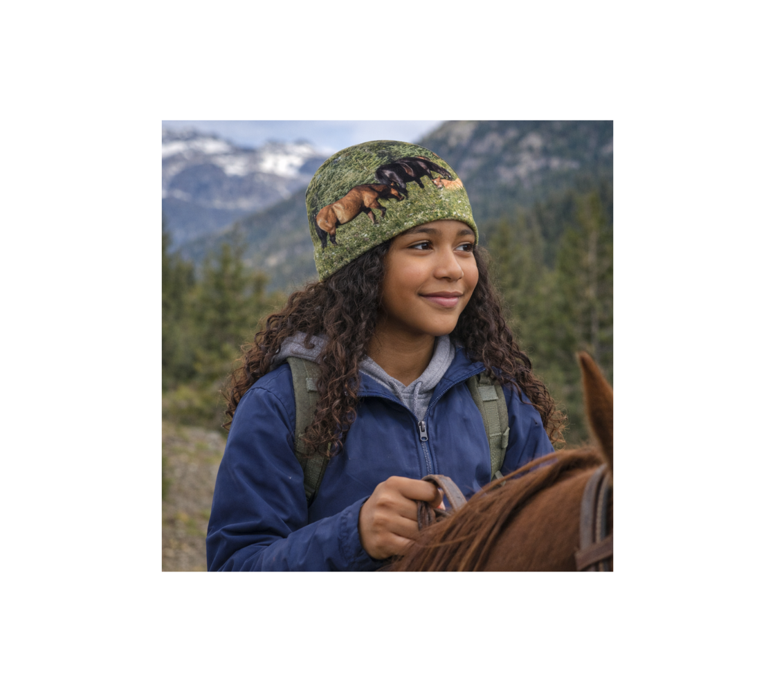 A young girl riding a horse wearing a bamboo-lined beanie with an image of wild horses design with a green background.