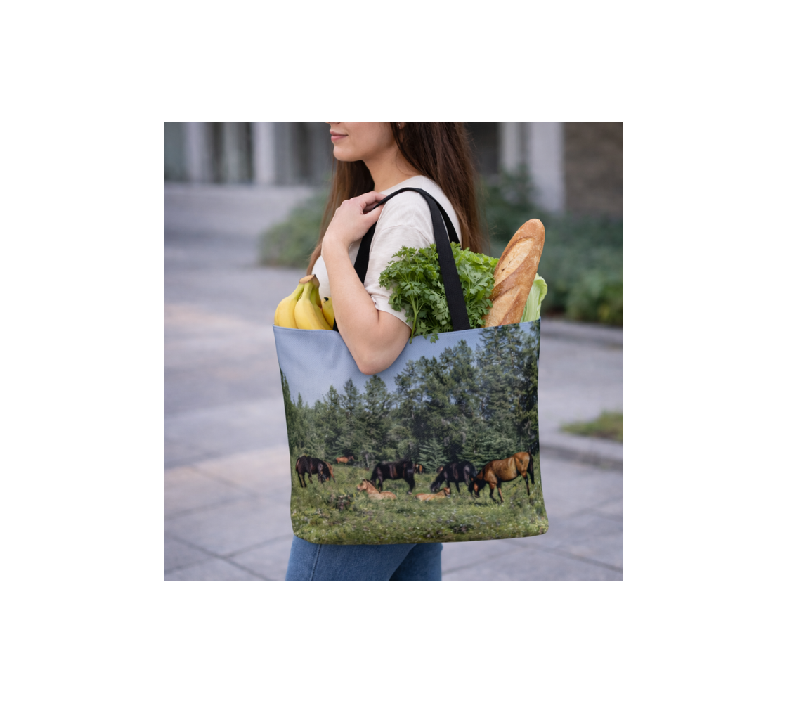 A woman carrying a large reusable tote bag with an image of a herd of wild horses design with a blue and green background filled with groceries.