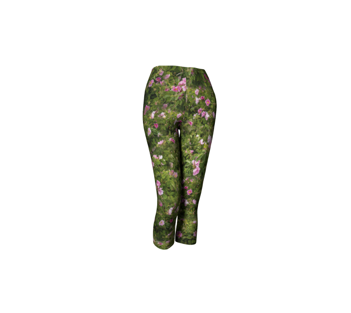 This is a front profile of a pair of 3/4 length wild rose capri leggings. The print is a photo collage of green wild rose bushes with pink flowers and buds througout that have yellow centers.