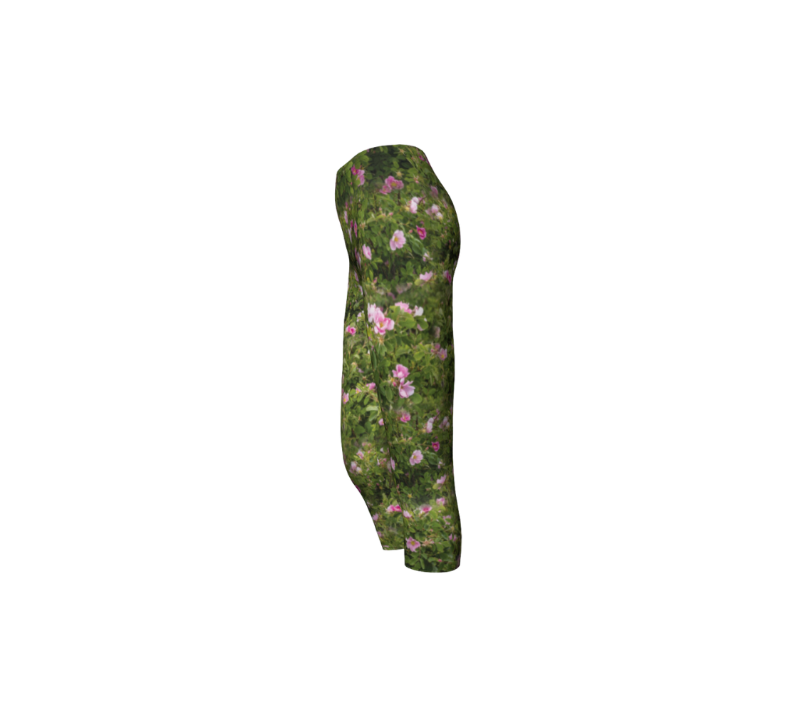 This is a side profile of a pair of 3/4 length wild rose capri leggings. The print is a photo collage of green wild rose bushes with pink flowers and buds througout that have yellow centers.