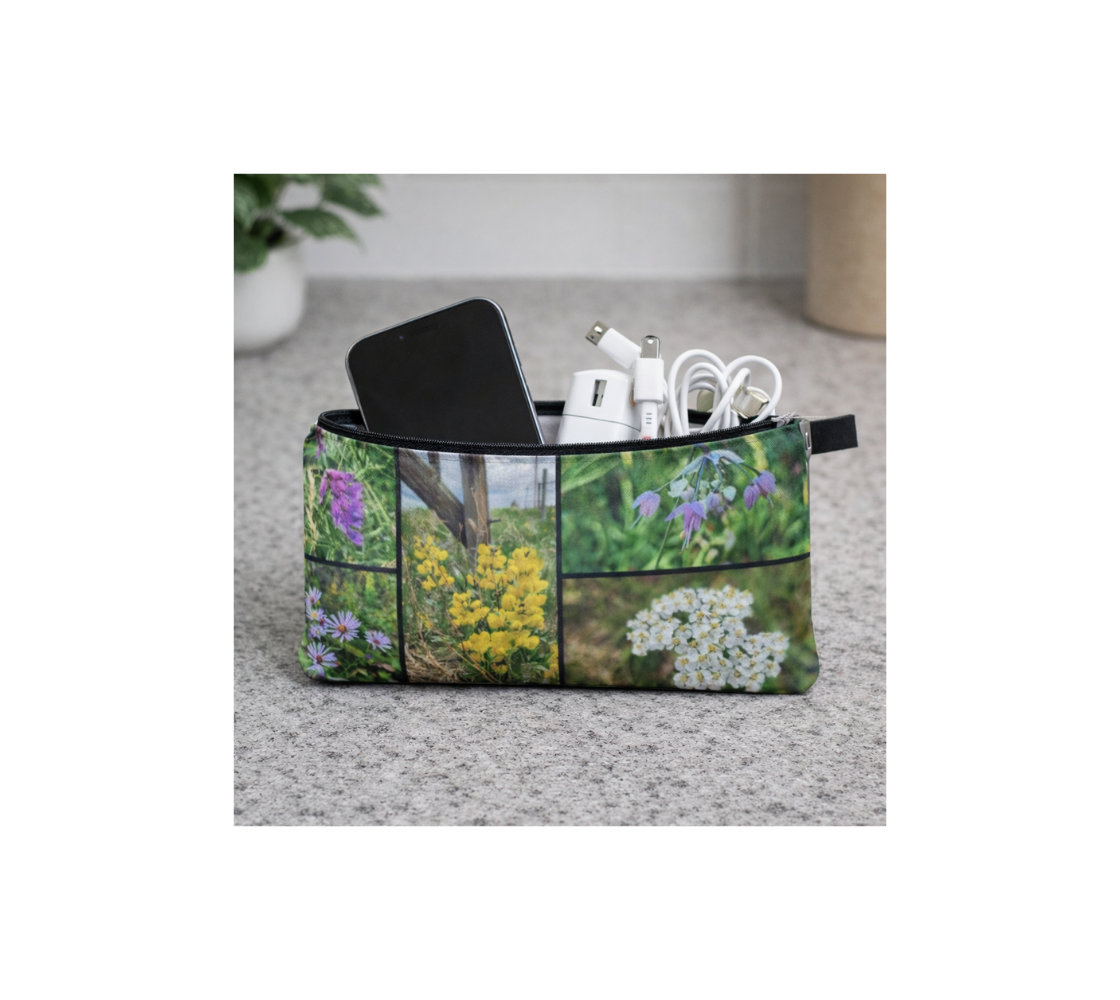 A zippered pouch with a collage of our photographs of wildflowers design with a cell phone and charging cord inside it.