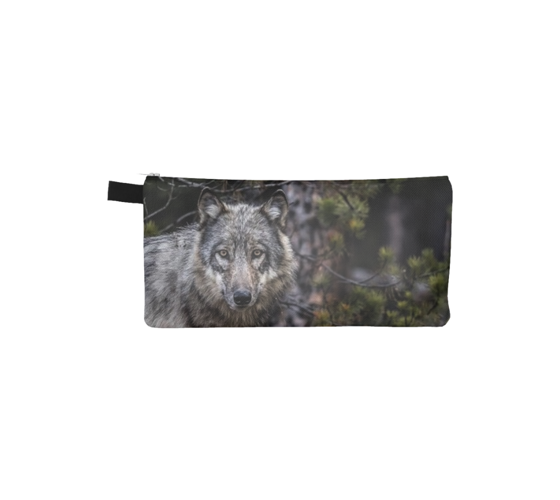 This is a front profile photo of a wolf 's head on a canvas zippered pouch. The background is of evergreen trees and grey bushes, while the wolf's coat is full and fluffy in various tones of grey, white and black with beautiufl yellow eyes looking directly at you.