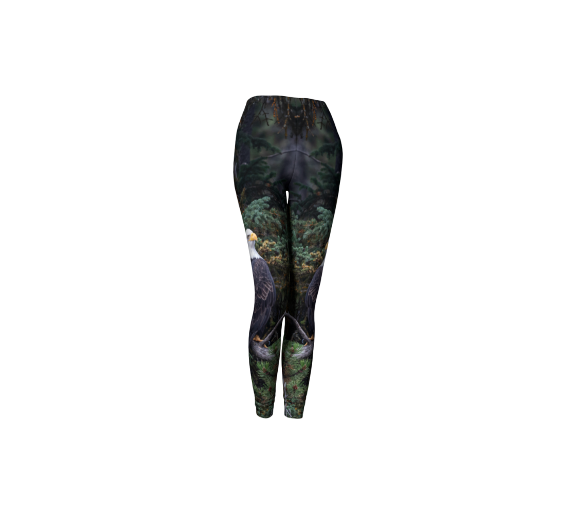 This is a front profile of a pair of classic leggings featuring a photo of a bald eagle on each leg, with a 1.5 inch wide elastic waistband. The background is of trees and branches in various tones of green, gold, purple and grey. The bald eagle is perched on a fallen grey tree trunk with his back to us and its head is turned slightly, as he is looking towards you.
