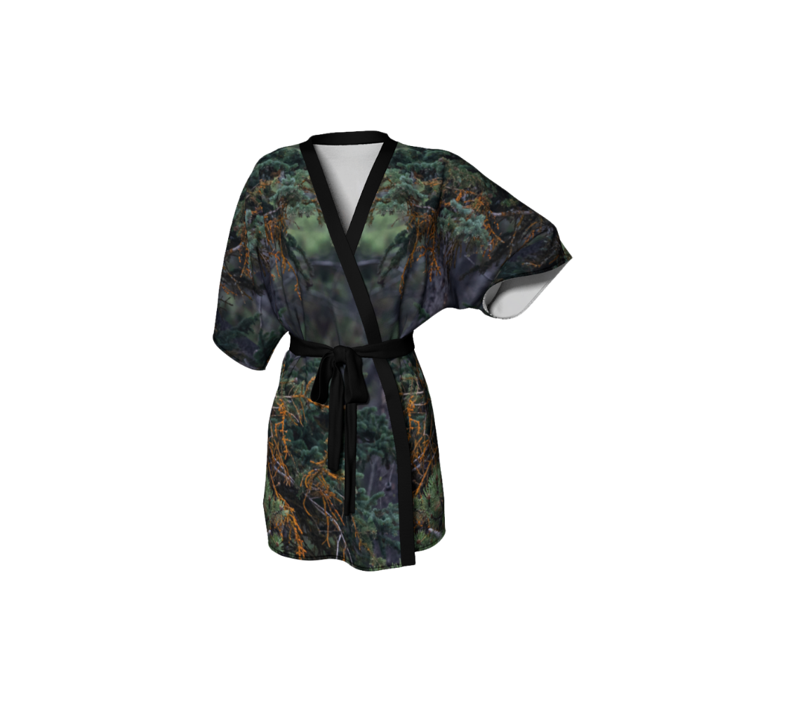 This frontview is a semi-sheer poly chiffon kimono robe, featuring a photo of the foilage that was around the bald eagle that is on the back of this kimono robe. The background is of pine trees with muted colors of teal, rust and and green throughout. Kimono has black trim and a black lightweight bamboo belt for tying.