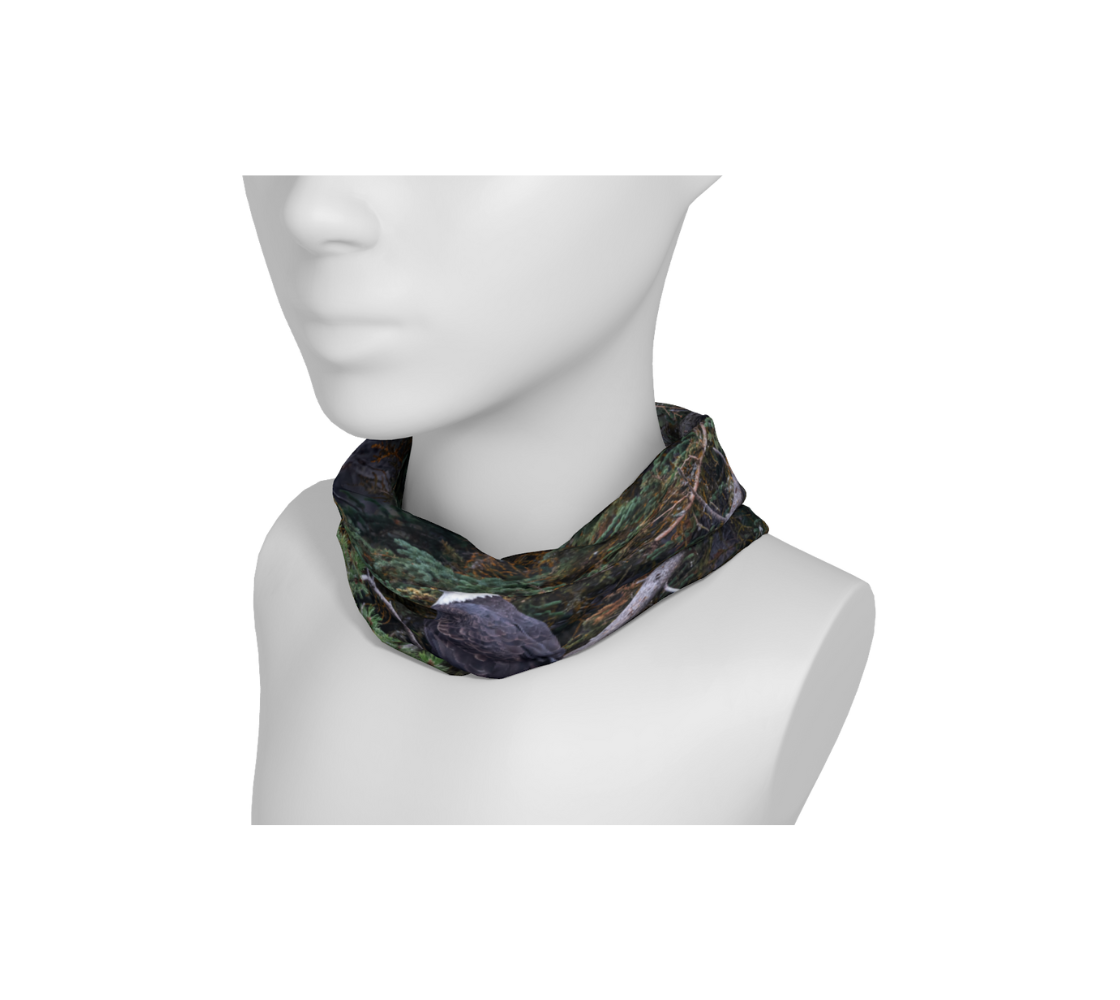 This is an image of a photo of a bald eagle on a neckband on a mannequin. The background is of trees and branches in various tones of green, gold, purple and grey. The bald eagle is perched on a fallen grey tree trunk with his back to us and its head is turned slightly, as he is looking towards you.