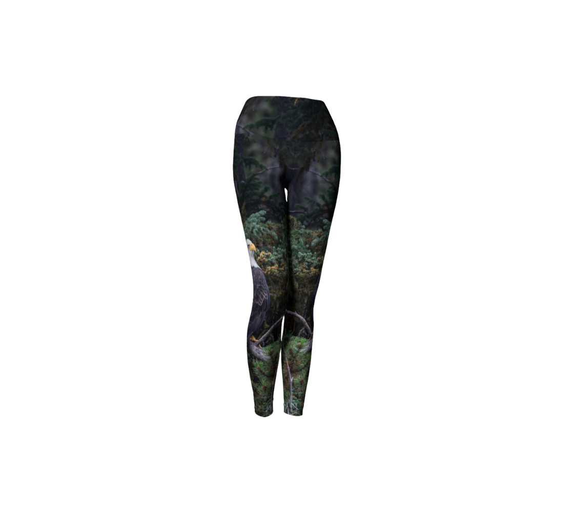This is a front profile of a pair of yoga leggings featuring a photo of a bald eagle on each leg, with a 4.5 inch wide waistband. The background is of trees and branches in various tones of green, gold, purple and grey. The bald eagle is perched on a fallen grey tree trunk with his back to us and its head is turned slightly, as he is looking towards you.