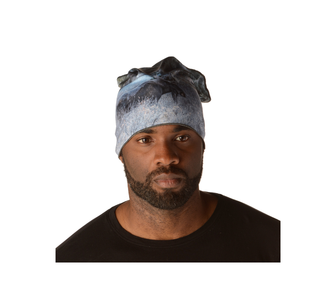 This is a image of a man wearing a photo of a bull moose on a head and neck band, worn as a kerchief. The fabric print shows a big dark brown bull moose standing in the frosty grey willows surrounded by evergreen trees. He is covered with a blanket of white frost on his back, shoulders and head.