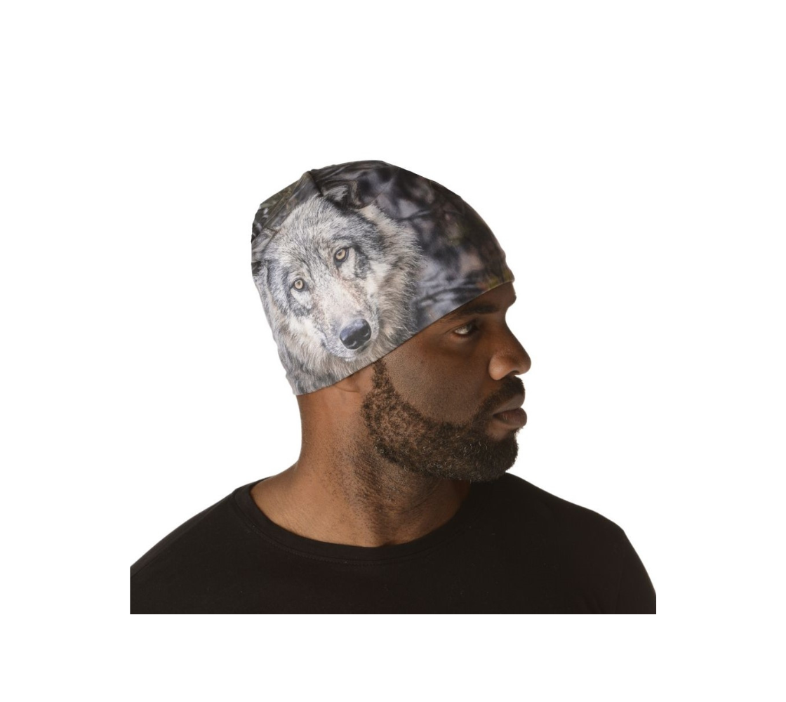 This is a side profile of a man wearing a beanie with a wolf head on it. It has one wolf head image on the front and one on the back. The background is of evergreen trees and grey bushes, while the wolf head is full and fluffy in various tones of grey and white with beautiufl yellow eyes looking directly at you.