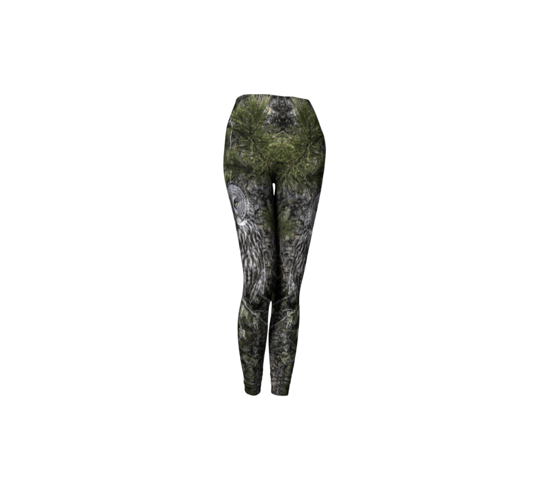 This is a side profile of a pair of classic leggings featuring a photo of a great grey owl on each leg, with a 1.5 inch wide elastic waistband. The background is green pine boughs and lichen hanging from the grey pine tree branches, with a great grey owl with black, grey and white feathers, and yellow eyes, perched on a branch.