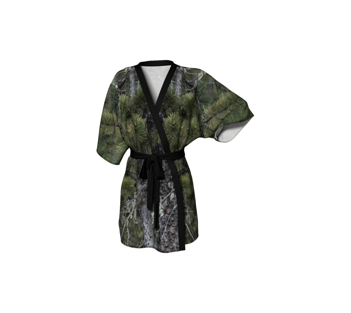 This frontview is of a semi-sheer poly chiffon kimono robe of a photo of pine tree boughs. The background is green pine boughs and grey pine trees with a great grey owl perched on a branch. The kimono has black trim and a black lightweight bamboo belt for tying.