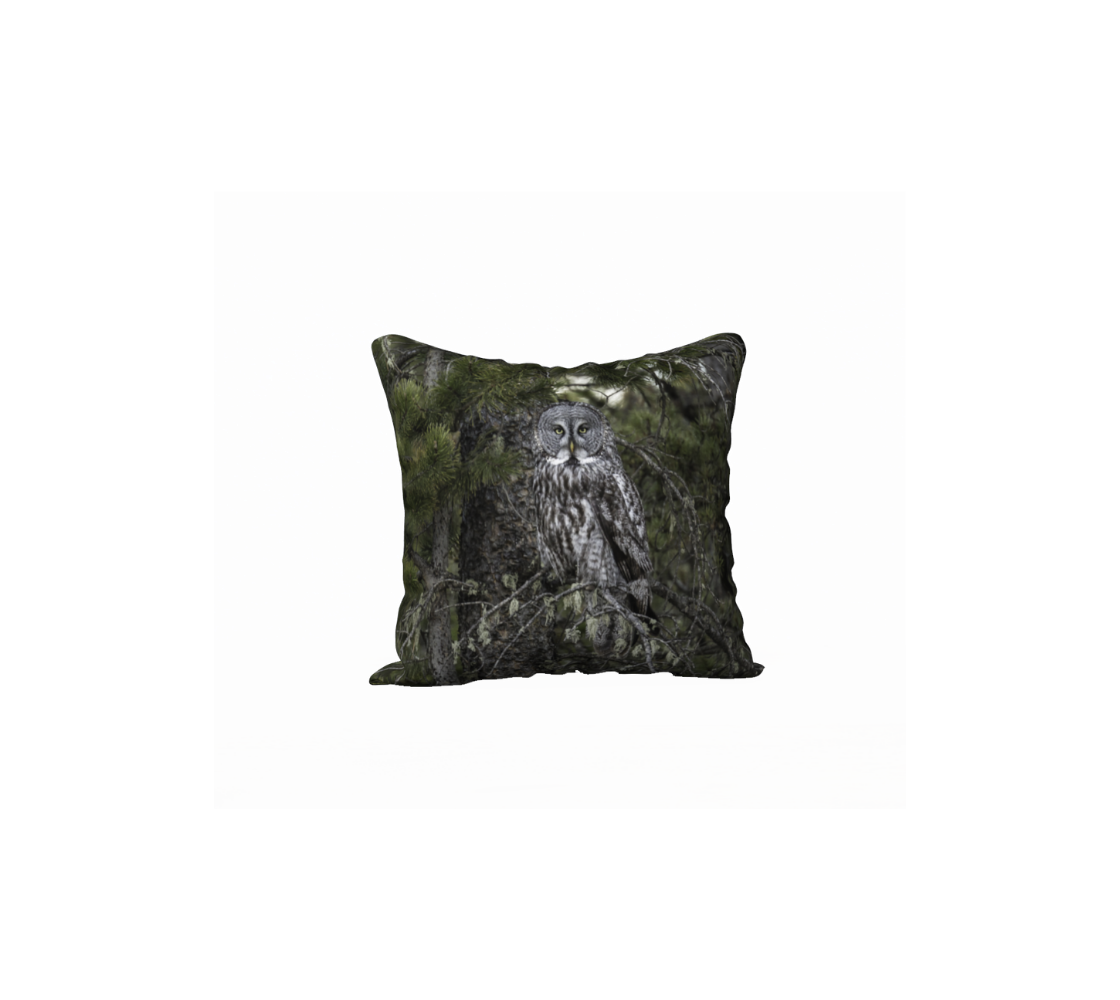 This 18 x 18 inch plush velveteen cushion cover features a photo of a great grey owl . The background is green pine boughs and lichen hanging from the grey pine tree branches, with a great grey owl with black, grey and white feathers, and yellow eyes, perched on a branch.