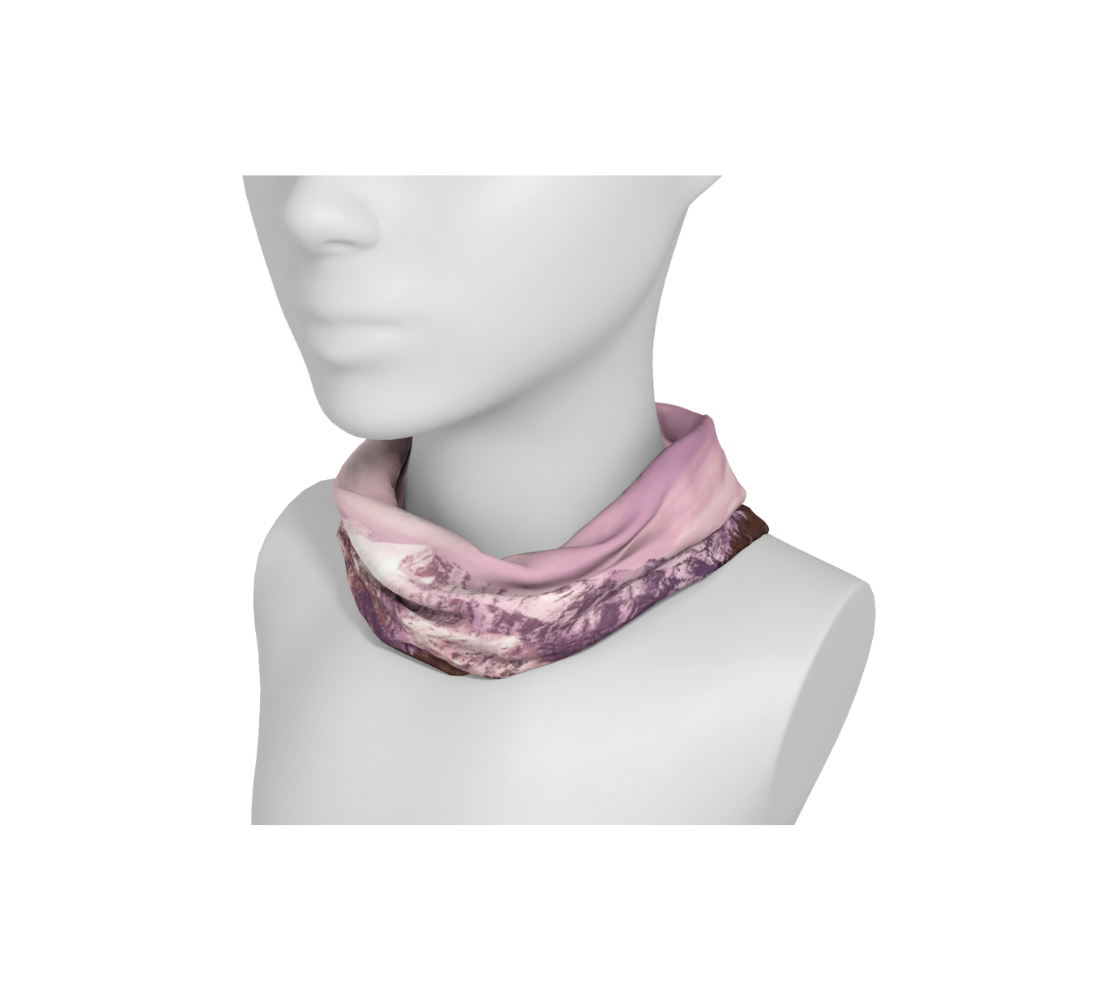 This is an image of a photo of a pink mountain scene on a head and neck band on a mannequin worn as a neckband. The scene is of a snow covered mountain in the far distance with a meandering stream winding its way through the fall colored willow and forest of evergreen trees towards the mountain. A special filter used when taking this photograph created an over all pink hue to the image that really accentuated the sunset light at the time.