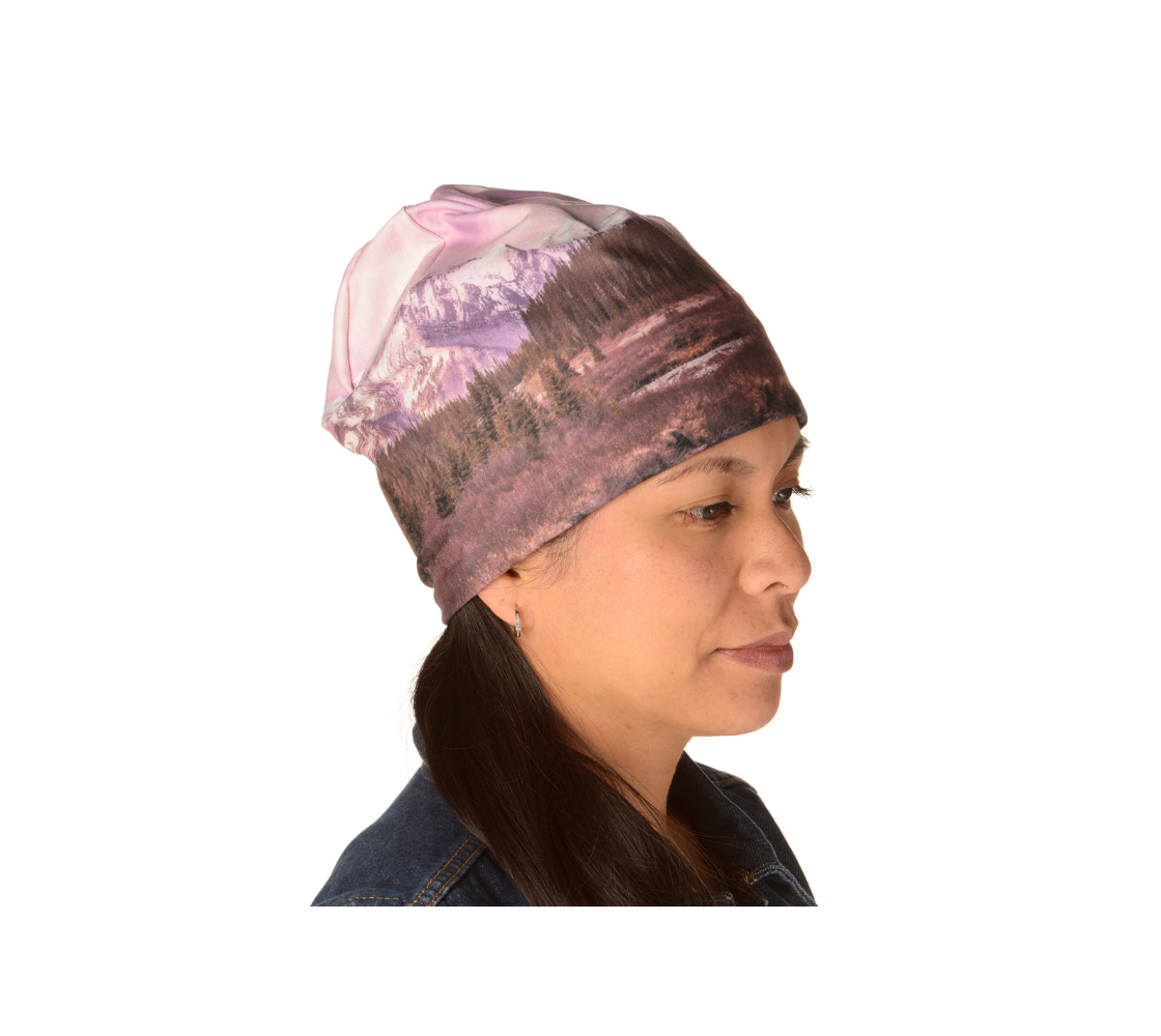 A photograph of a pink mountain sun set on a beanie. A lady wearing the  beanie with the pink tones. Available in adult or youth sizes small-medium or large-extra.