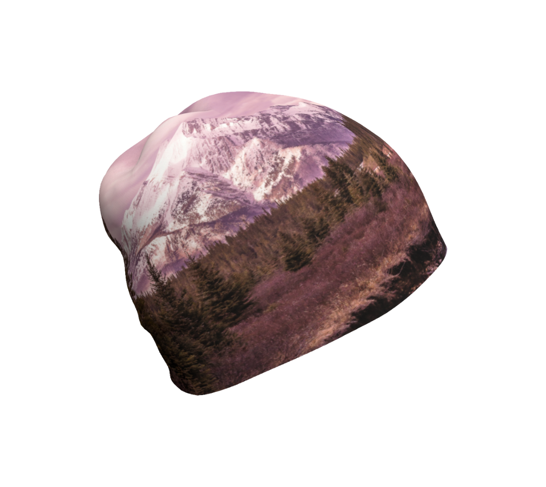 This is a photograph of a pink mountain sunset on a beanie. The image is of a snow covered mountain in the far distance with a meandering stream winding its way through the fall colored willow and forest of evergreen trees towards the mountain. A special filter used when taking this photograph created an over all pink hue to the image that really accentuated the sunset light at the time.