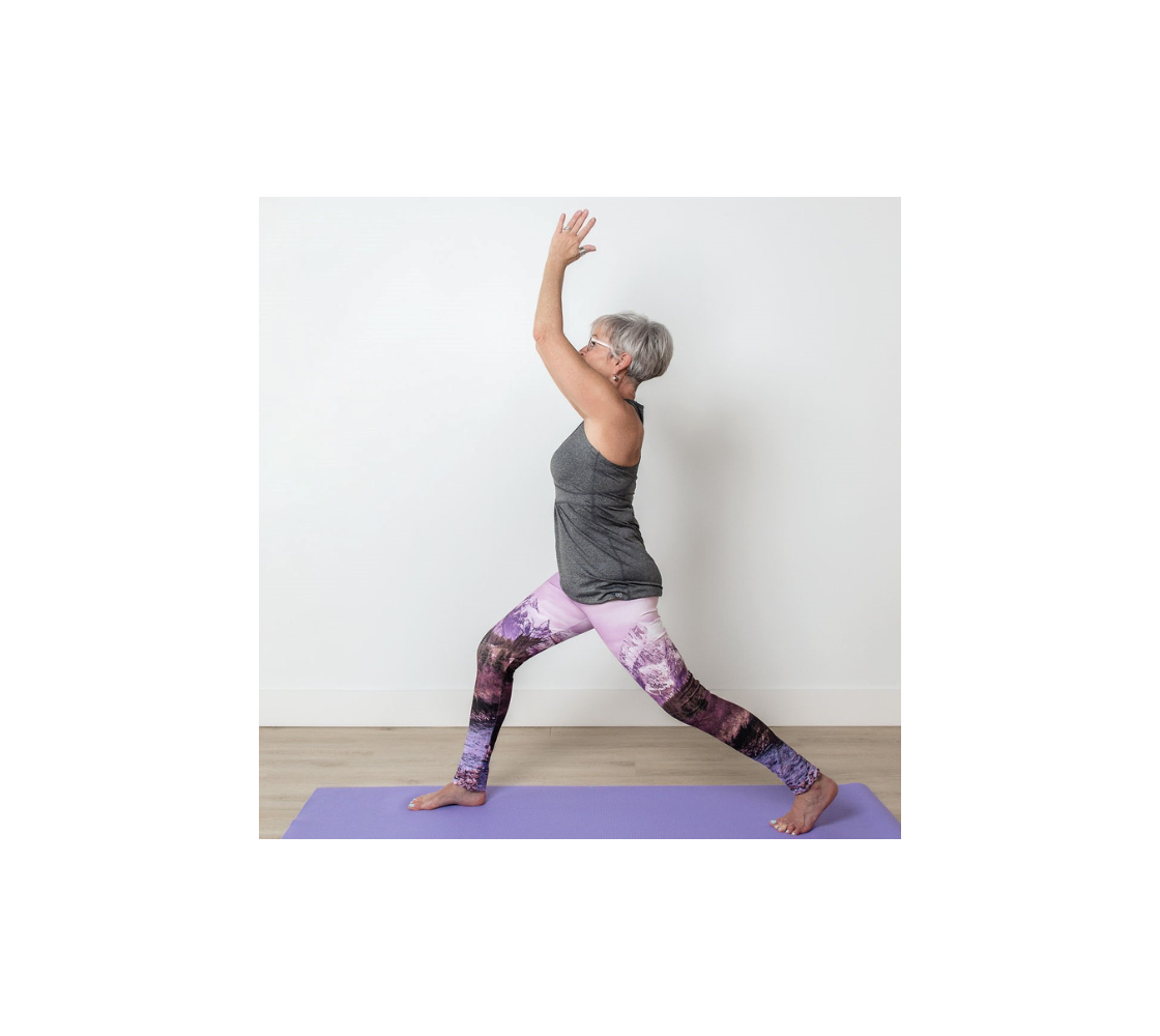 This is a side profile of a lady doing a yoga pose in a pair of yoga leggings featuring a photo of a pink mountain scene. The image is of a snow covered mountain in the far distance with a meandering stream winding its way through the fall colored willow and forest of evergreen trees towards the mountain. A special filter used when taking this photograph created an over all pink hue to the image that really accentuated the sunset light at the time.