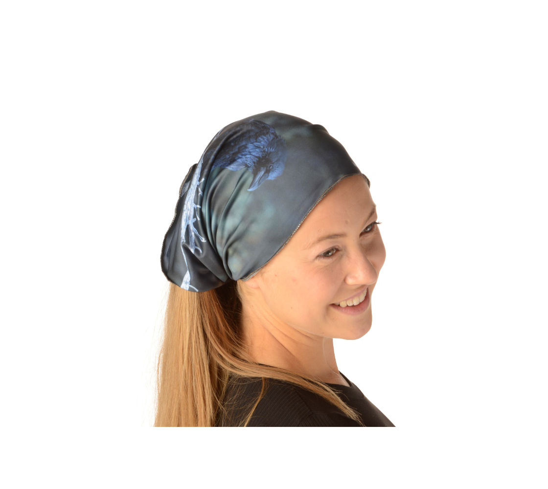 This is a photograph of girl wearing a photo of a raven's head on a head and neck band worn as a kerchief. The background is mottled green with the raven's head in various tones of dark blue as the sun reflects its colors.