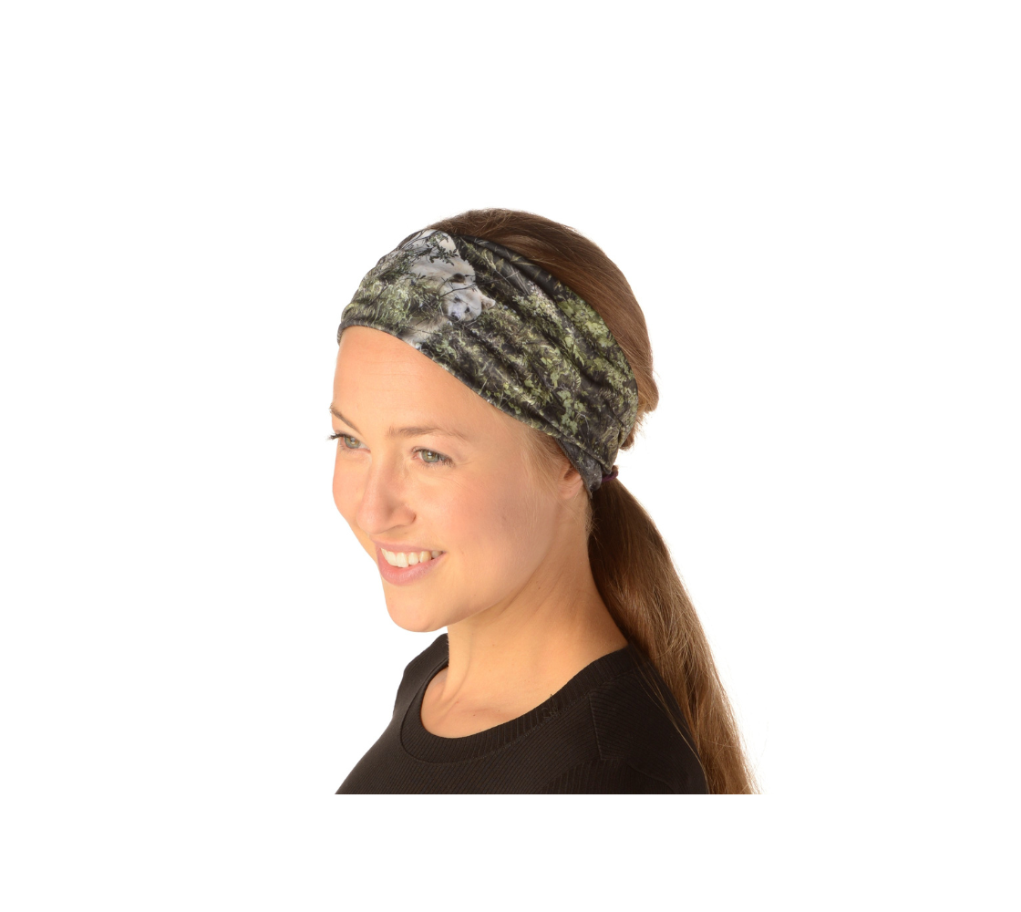 This is an image of lady wearing a photo of a spirit bear on a head and neck band worn as a headband. The background is green bushes and brown branches of the Great Bear Rainforest. The white spirit bear is stepping down out of the forest and is making her way to the stream below.