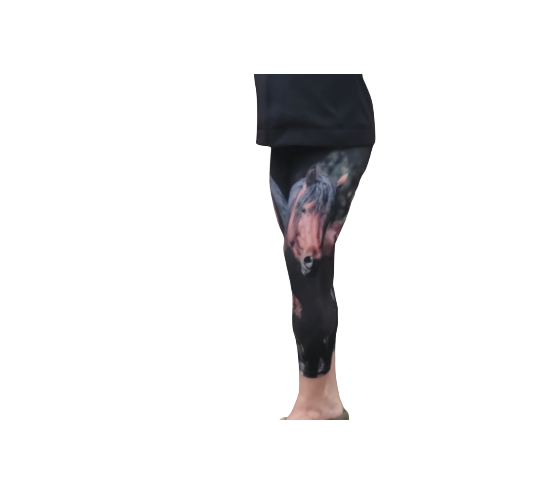 An image of a girl wearing a photo of a wild stallion on 3 quarter length capris. The background is dark green/black at the top with green grass at the bottom, with an portrait image of a chestnut brown wild horse with a black mane and tail.