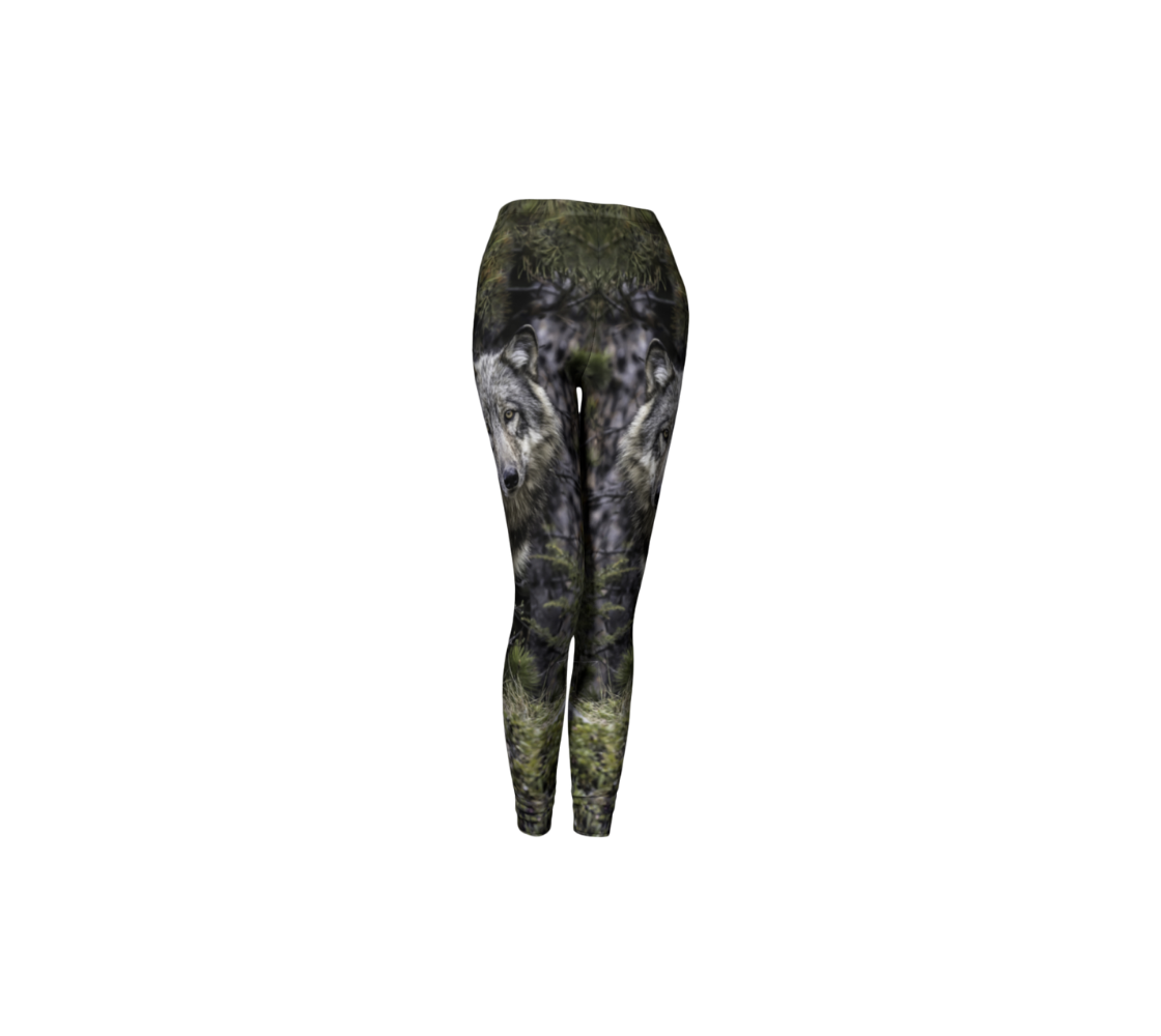 This is a front profile of a pair of classic leggings featuring a photo of a wolf on each leg, with a 1.5 inch wide elastic waistband. The background is of evergreen trees and grey bushes, while the wolf's coat is full and fluffy in various tones of grey, white and black with beautiufl yellow eyes looking directly at you.