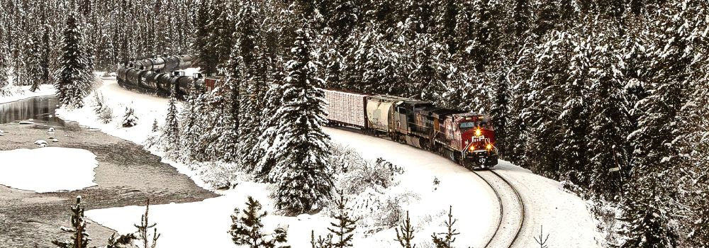 A long freight train with a bright red engine passing along Morant's Curve an iconic snow-covered winter scene along the Bow River in the Rocky Mountains.