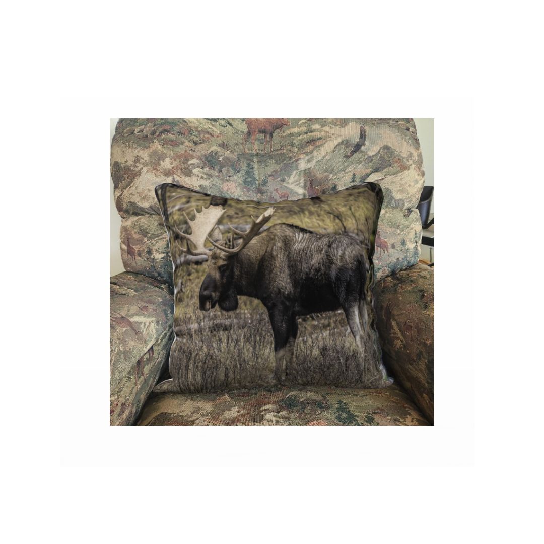 A 18 x 18 inch plush velveteen cushion cover featuring a bull moose in autumn and the background is golden and green. This image is of a cushion cover on pillow form in a chair.