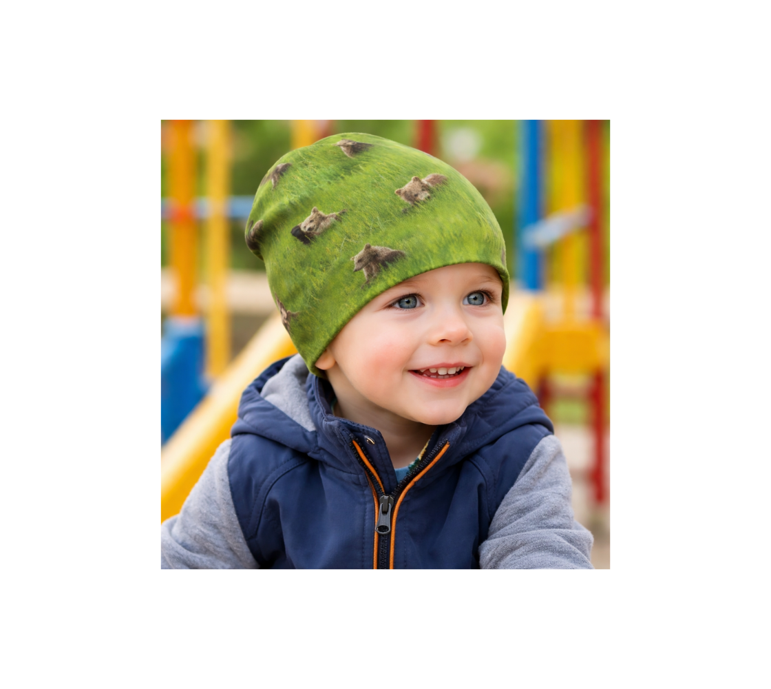 A Toddler at play ground wearing a bamboo-lined beanie with collage of brown bears cubs  design with a green background. 