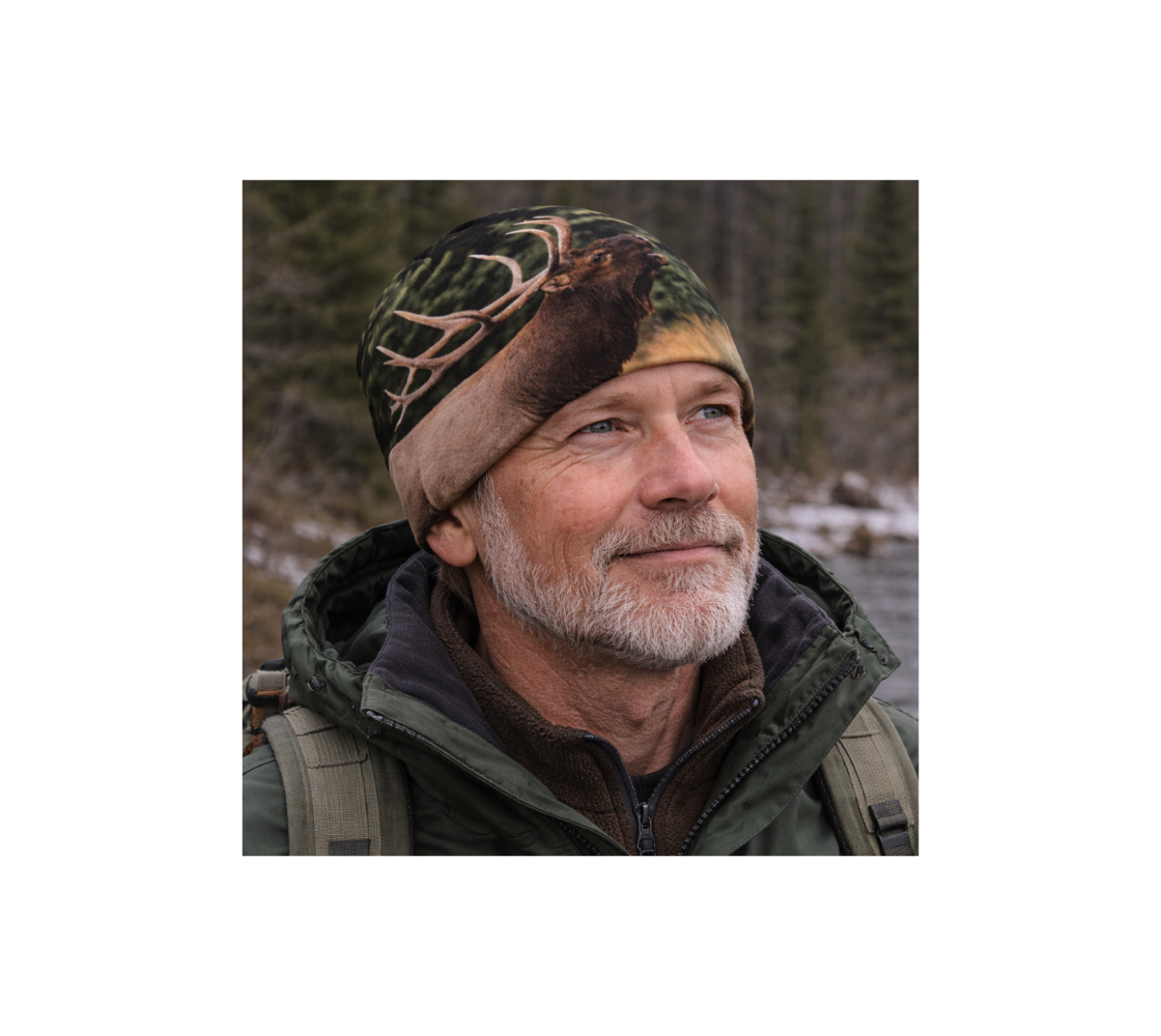 A Older man standing by river wearing a bamboo-lined beanie with an image of bull elk design with a green background.