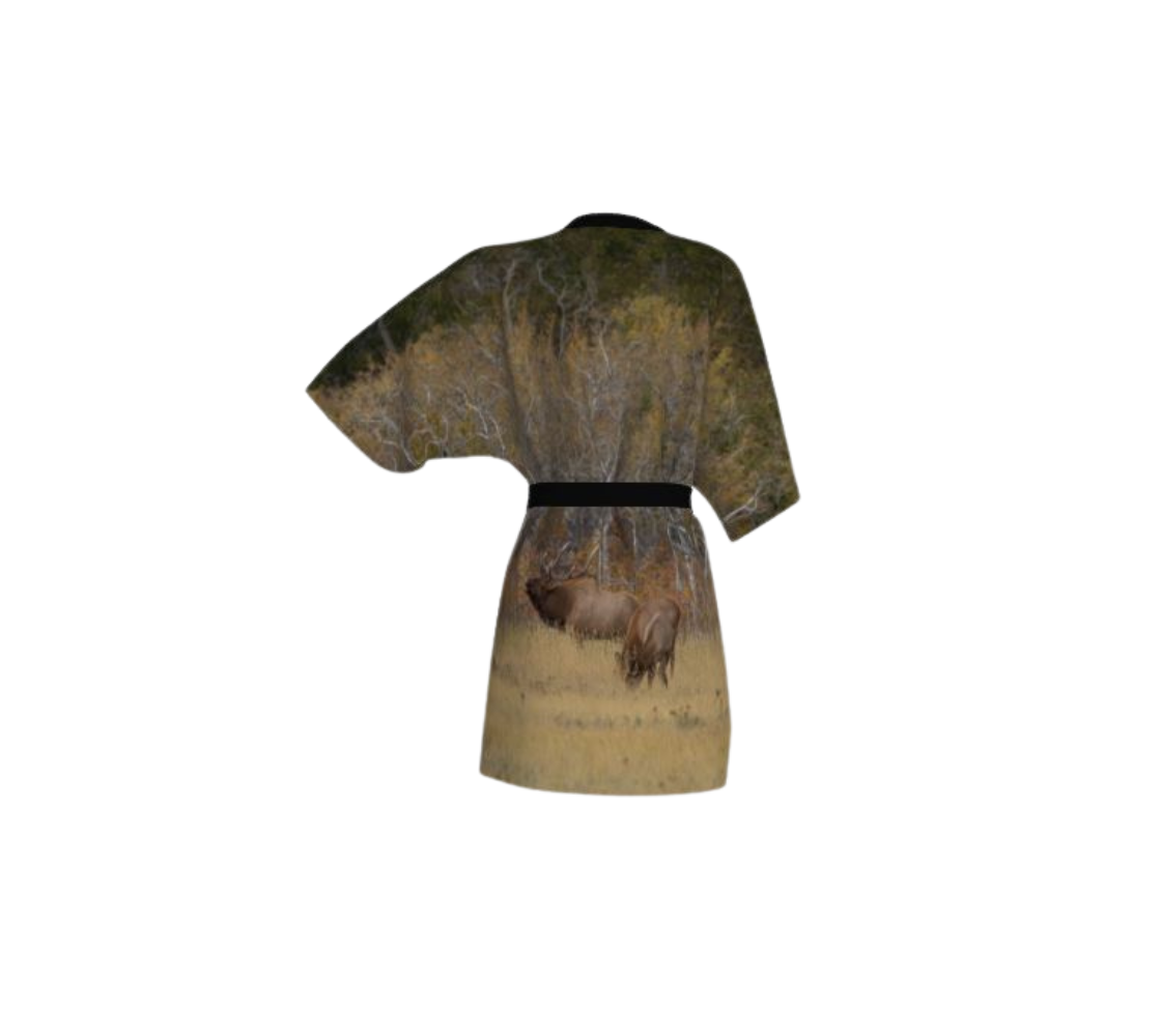 This backview is a semi-sheer poly chiffon kimono robe featuring a photo of a bull elk. Background is yellow and brown with blurred trees, with a bull and cow elk standing in golden colored grass. Kimono has black trim and a black lightweight bamboo belt for tyin