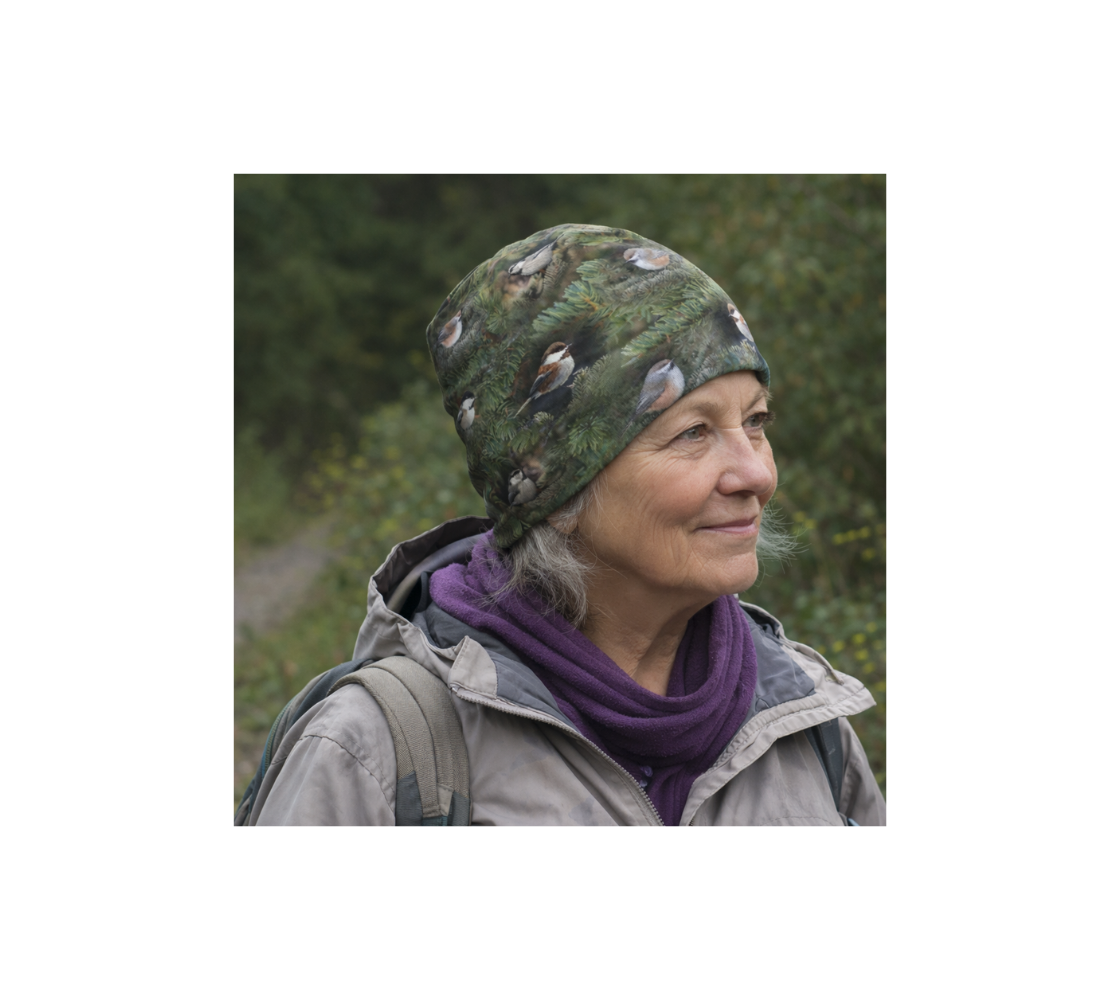 A elderly woman walk in nature wearing a bamboo-lined beanie with a collage of four different chickadees design with a green background.