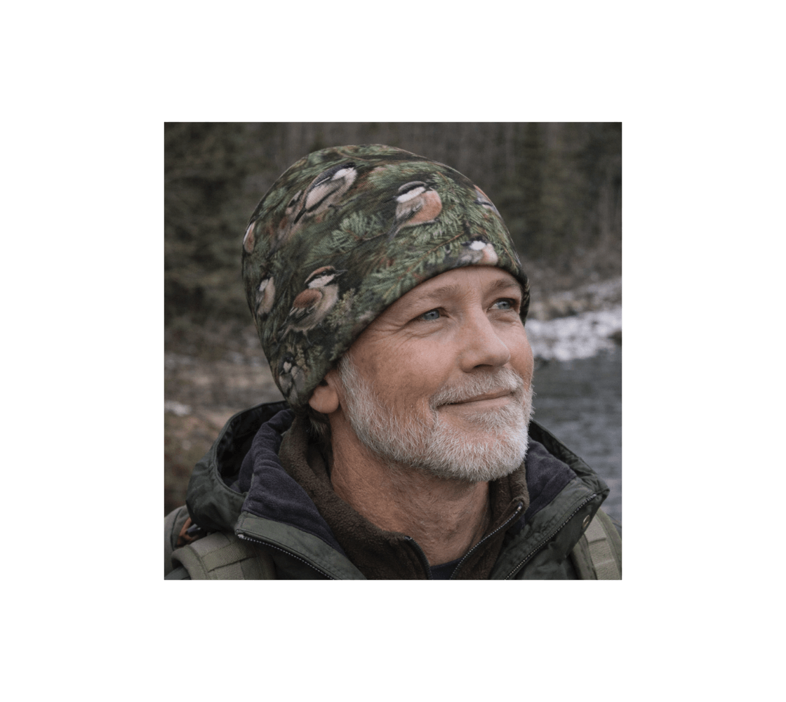 A elderly man wearing a chickadee bamboo-lined beanie from our wildlife photography standing by river.