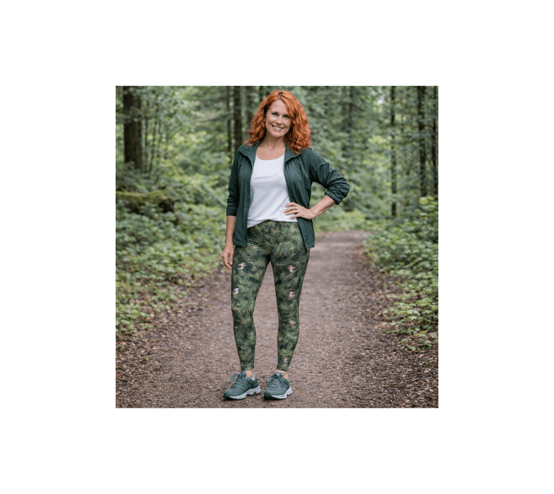 A woman wearing a pair of chickadee classic leggings from our real wildlife photography standing on a path in a forest.