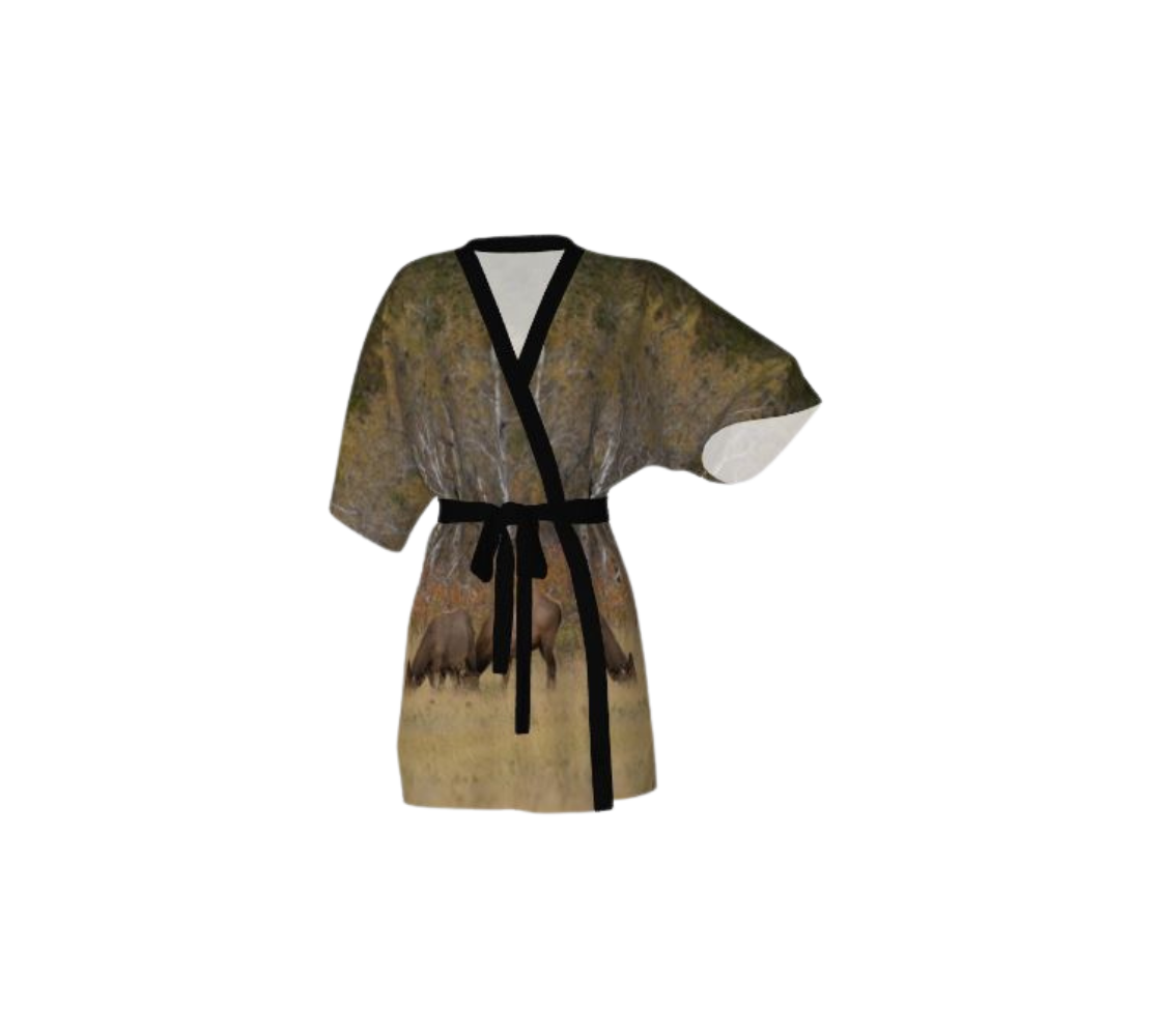 This frontview is a semi-sheer poly chiffon kimono robe featuring a photo of cow elk. Background is yellow and brown with blurred trees, with cow elk standing in golden colored grass. Kimono has black trim and a black lightweight bamboo belt for tying.