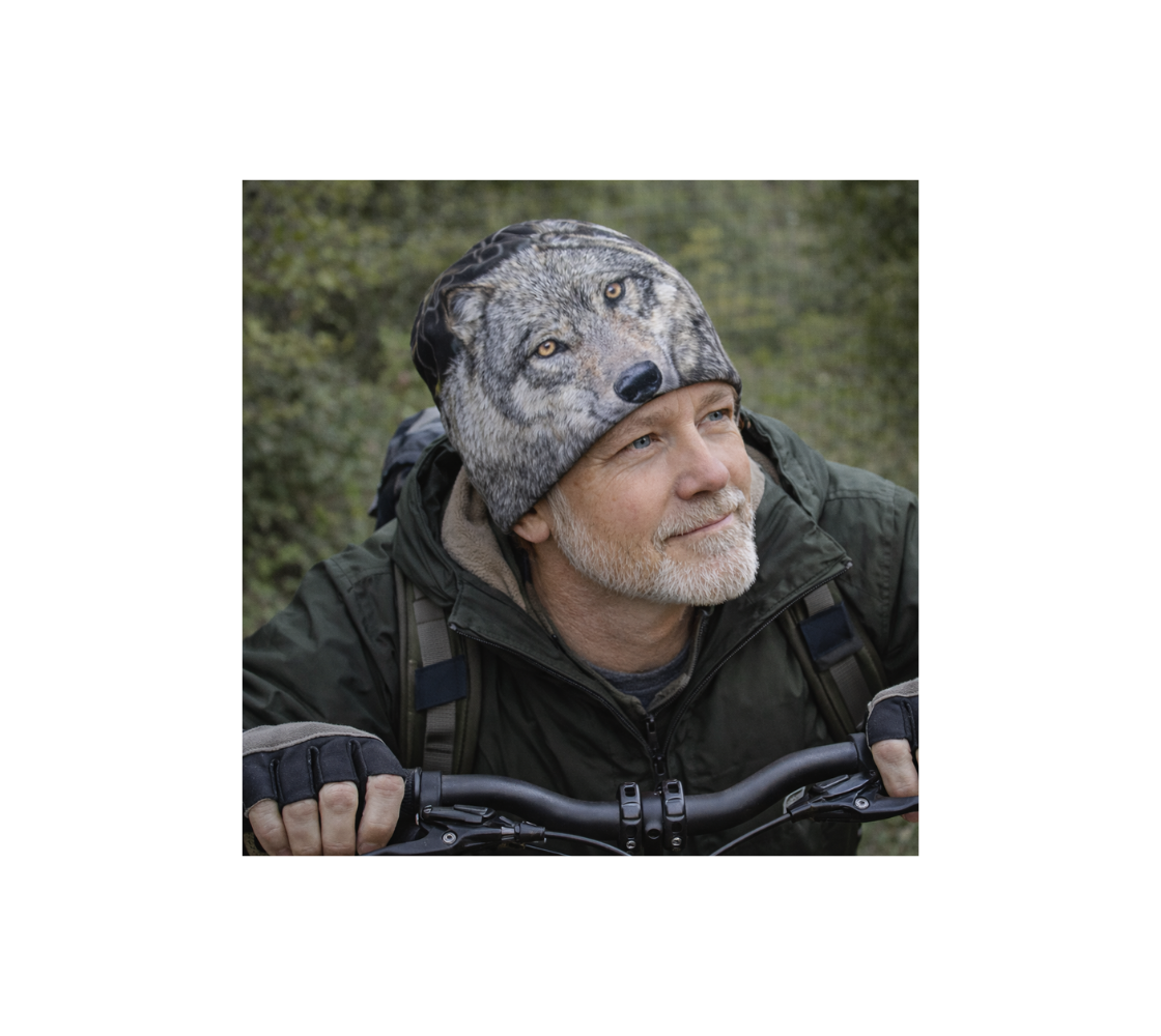 A elderly man riding bicycle wearing a beanie with an image of wolf.